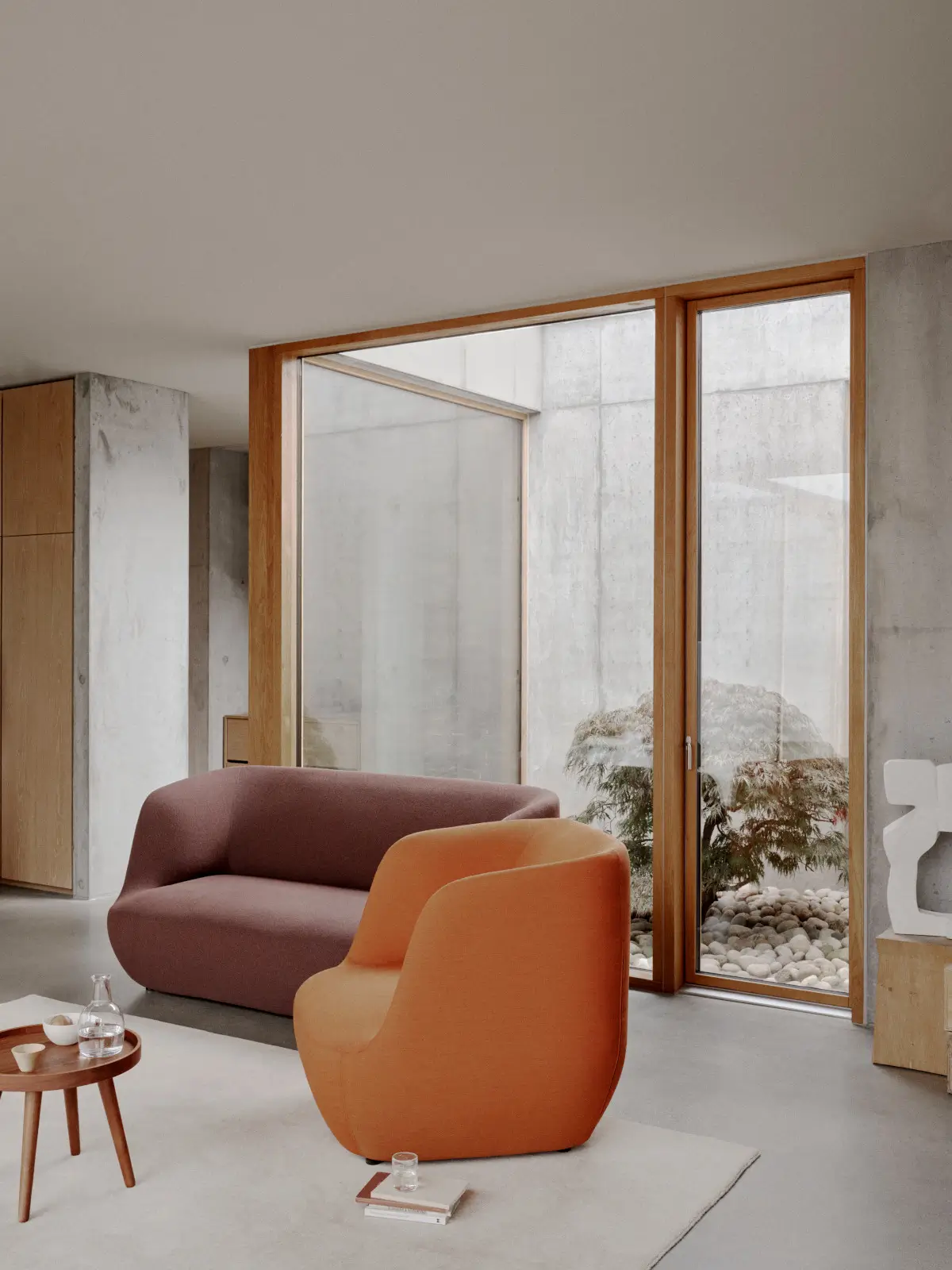 Softline Clay Loungesessel in Orange vor einem rosafarbenen Sofa in einem modernen Wohnraum mit großen Fenstern und natürlichem Licht.