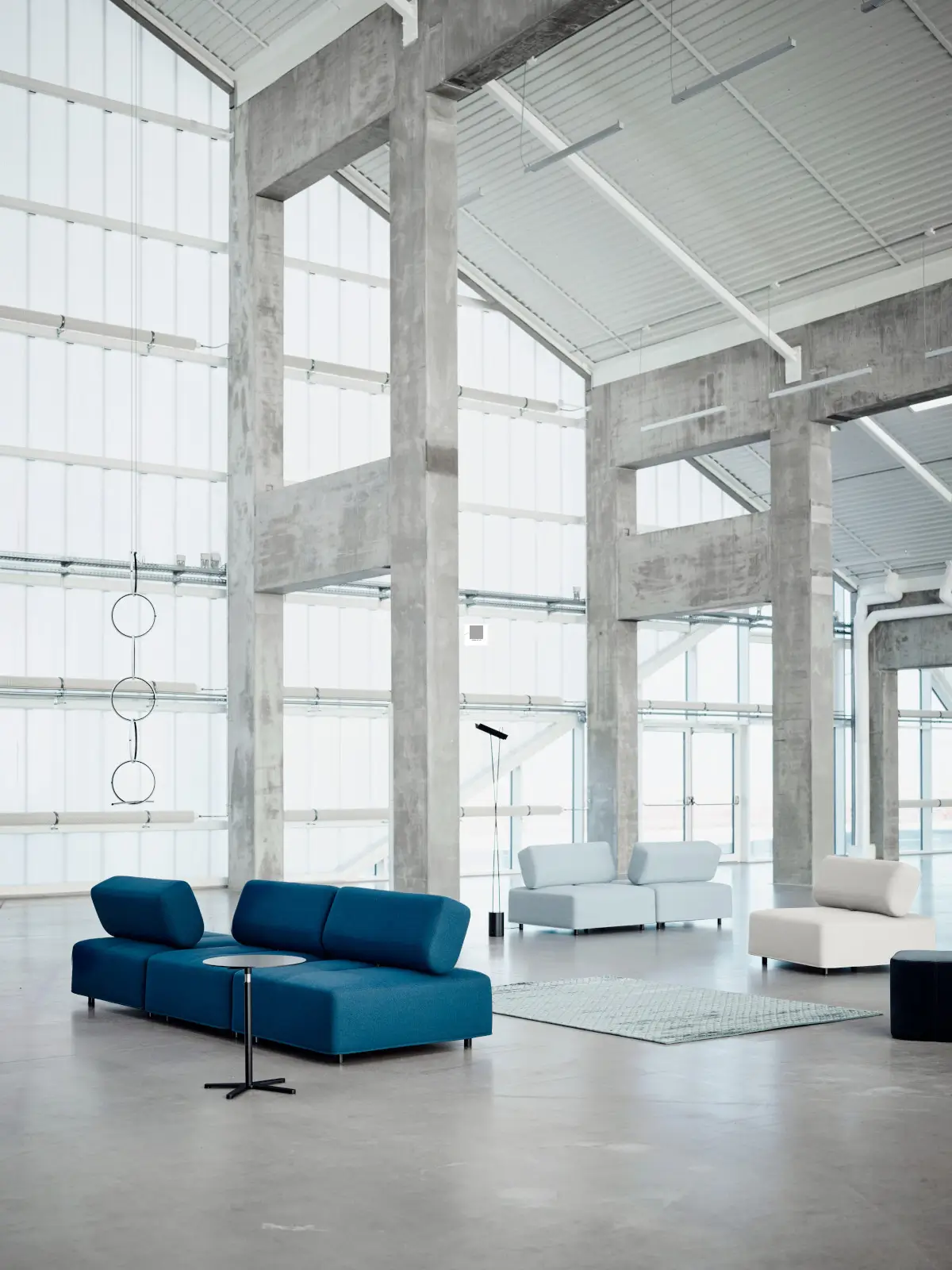 Softline Cabala Hocker und Sofaelemente in Blau, Hellgrau und Beige in einem großzügigen modernen Loft mit Betonarchitektur, Teppich und Beistelltischen.
