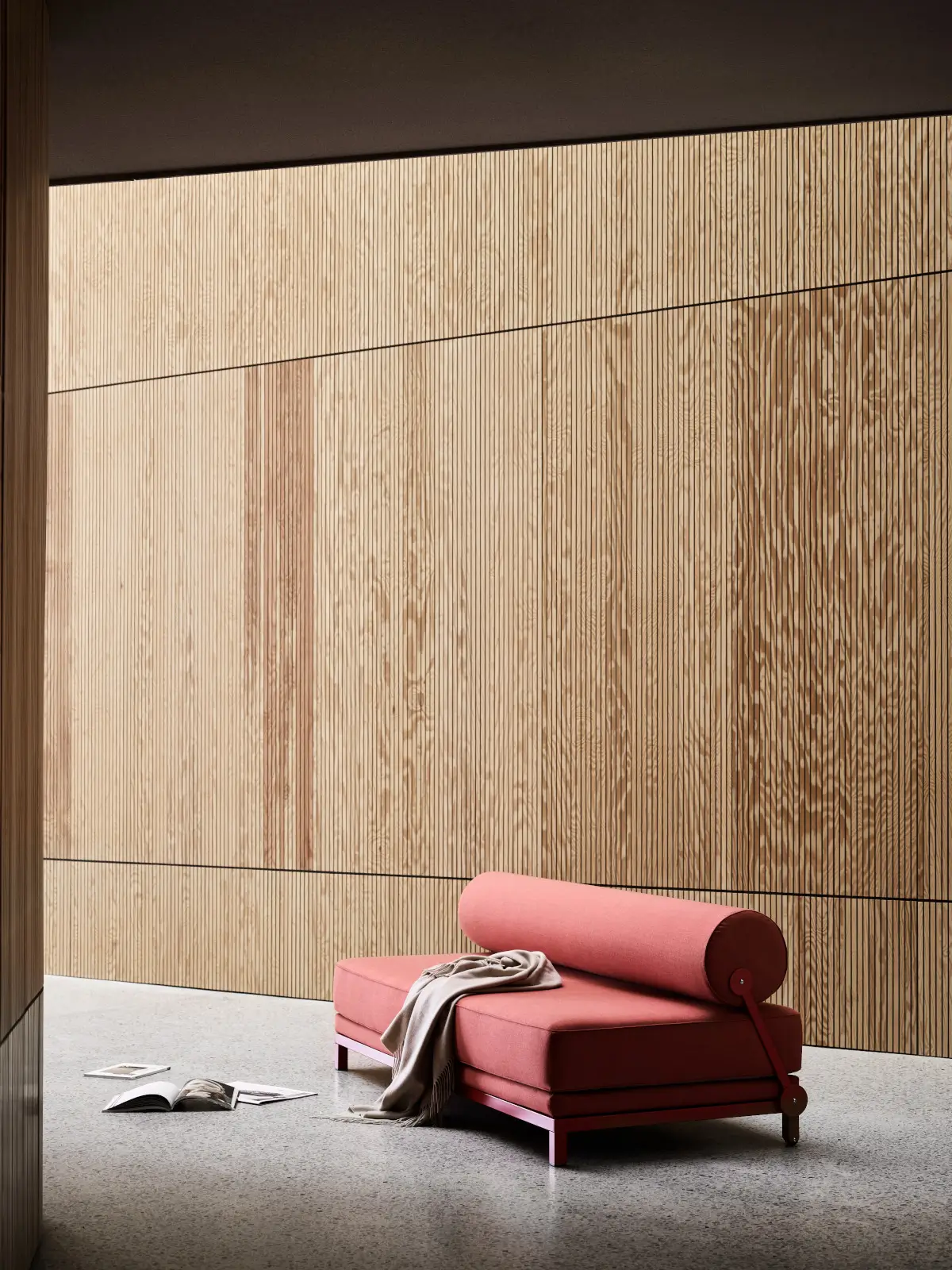 Softline Sleep Sofa in Rot in einem modernen Ambiente vor einer strukturierten Holzwand mit zylindrischer Rückenlehne, Metallgestell und Decke.