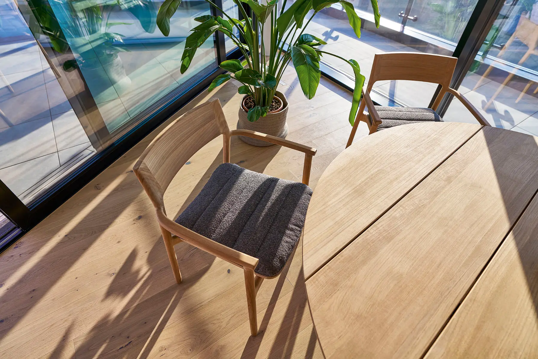 Weishäupl Teva Essgruppe mit rundem Teakholztisch Ø 140 cm und gepolsterten Sesseln in einem modernen Essbereich. Hochwertige Designmöbel für Wohn- und Outdoor-Bereiche.