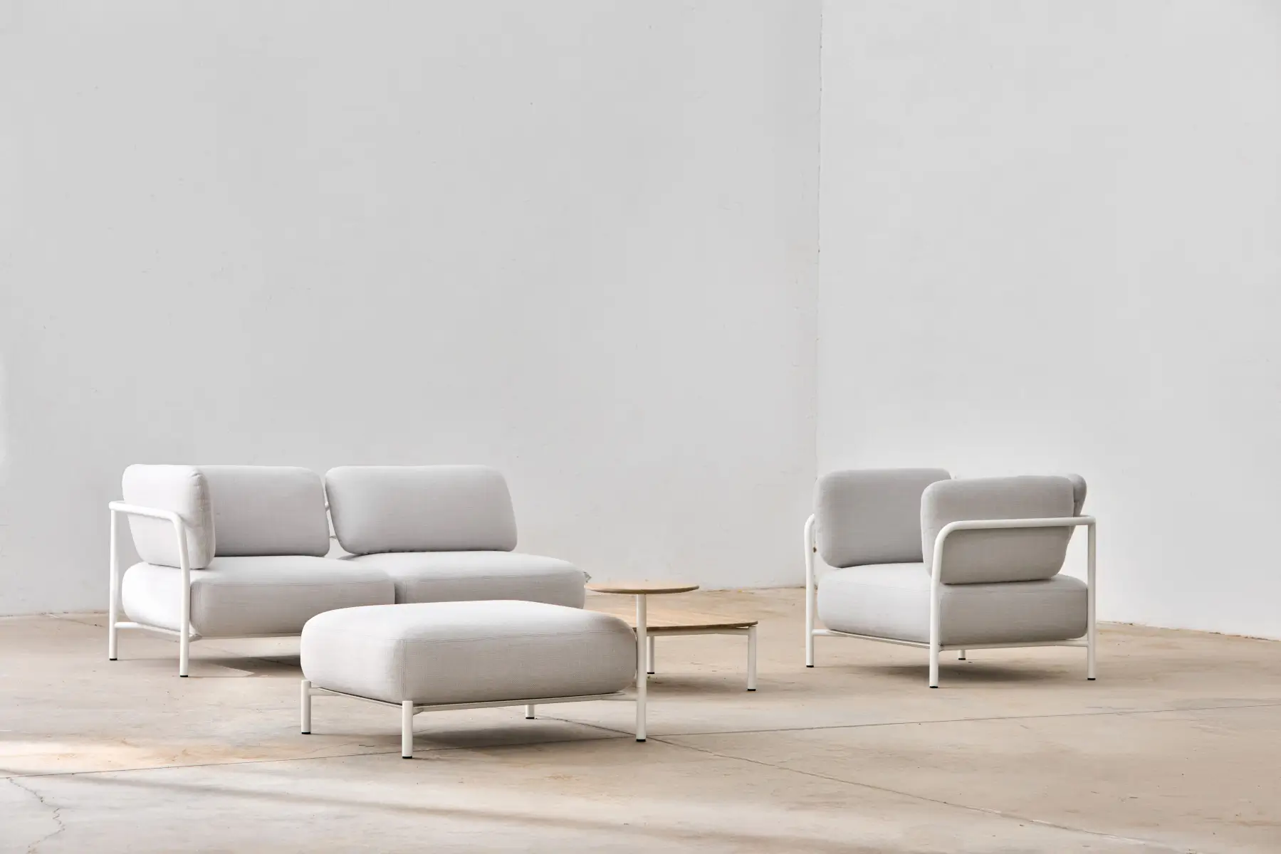 Softline Club Hocker in Hellgrau vor passendem Sofa und Sessel in einem hellen, minimalistischen Wohnambiente mit kleinen Beistelltischen.