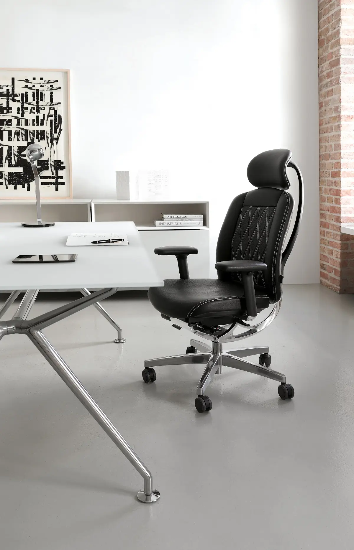 Wagner AluMedic Limited S Bürostuhl mit Kopfstütze, schwarzem Lederbezug und Aluminium-Fußkreuz an einem modernen Schreibtisch in einer hellen Büroeinrichtung.