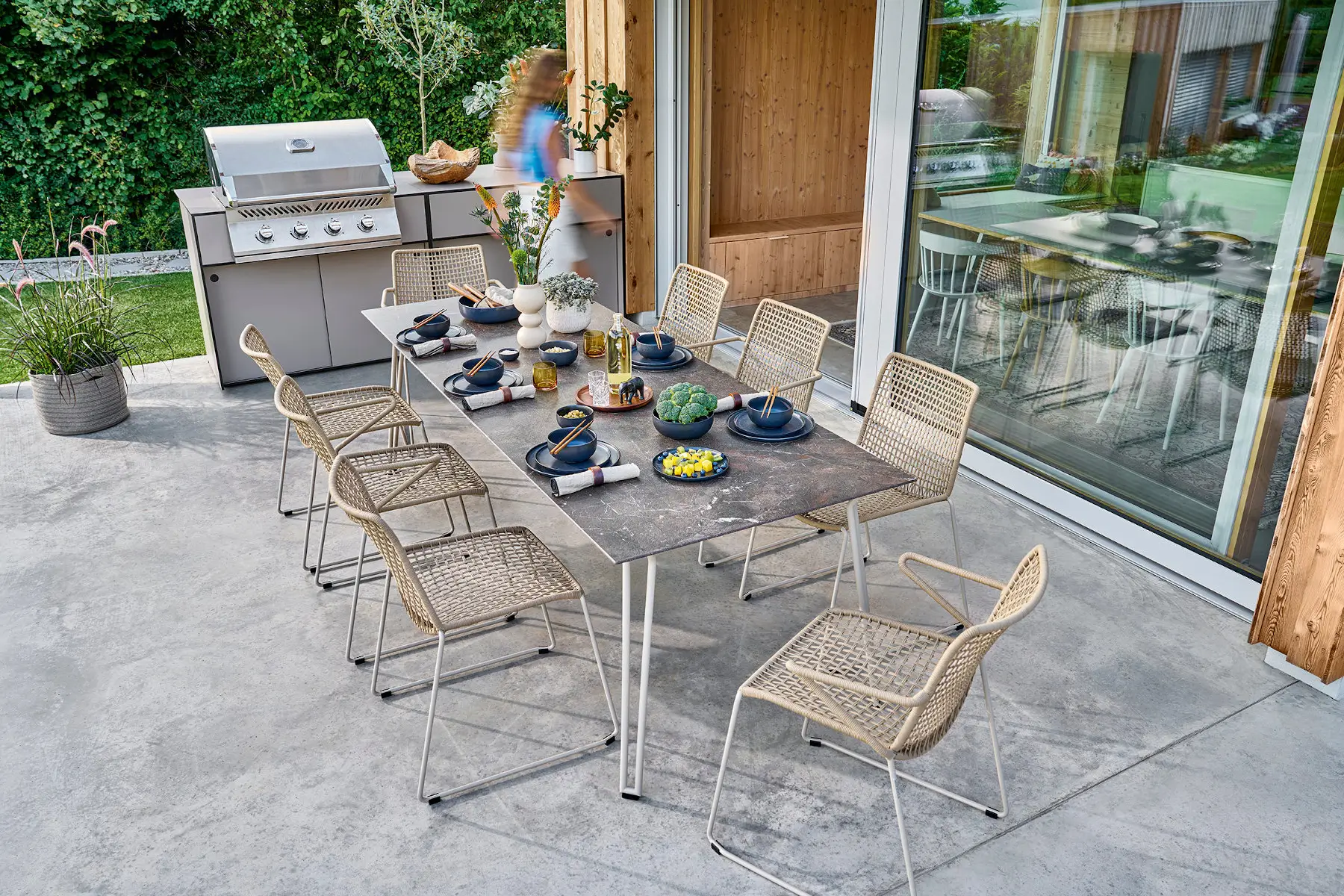 Weishäupl Slope Gartenstühle in Perlbeige mit Geflecht an großem Outdoor-Esstisch auf moderner Terrasse.