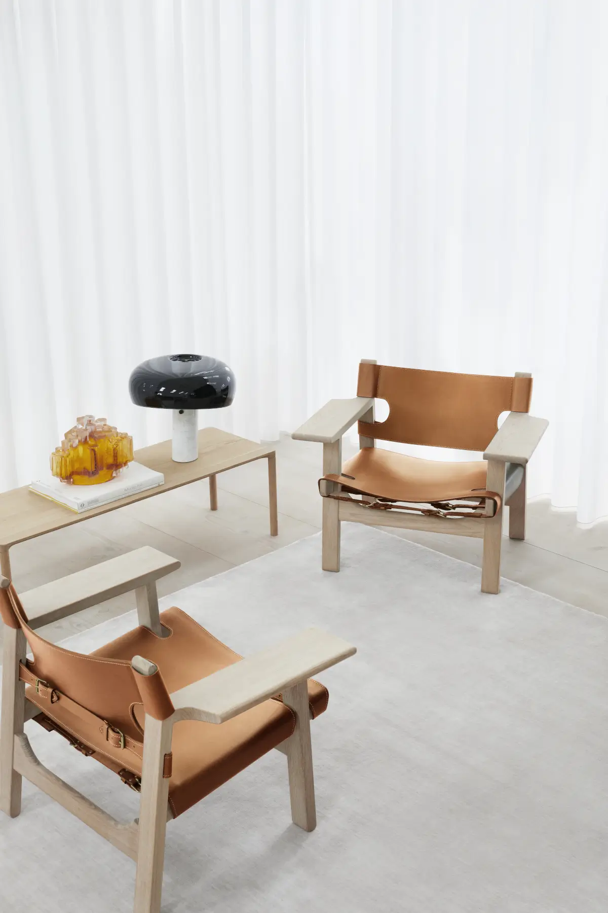 Heller Massimo Copenhagen Bamboo Teppich in einem modernen Wohnbereich mit zwei Ledersesseln, niedrigem Holztisch und weißen Vorhängen.