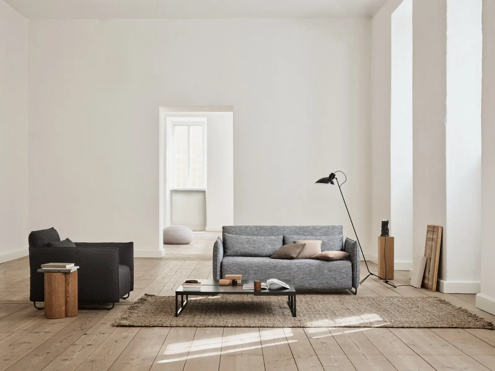 Softline Cord Sofa in Grau mit Rückenkissen und passenden Cord Sesseln in einem hellen Wohnzimmer mit Holzboden, Teppich und schwarzem Couchtisch.