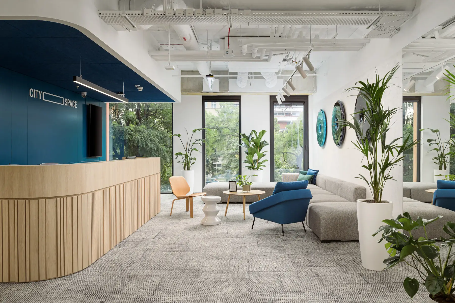 Blauer Noti Nome Sessel mit schwarzen Metallbeinen im hellen Empfangsbereich mit Lounge-Sofa, Holzmöbeln und großen Fenstern