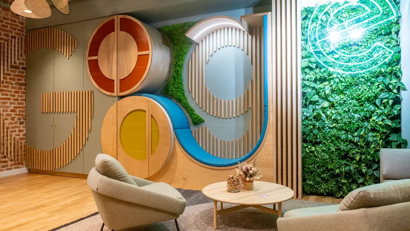 Beiger Noti Nome Sessel mit schwarzen Metallbeinen in einer modern gestalteten Google Büro-Lounge mit Holzelementen und grüner Pflanzenwand