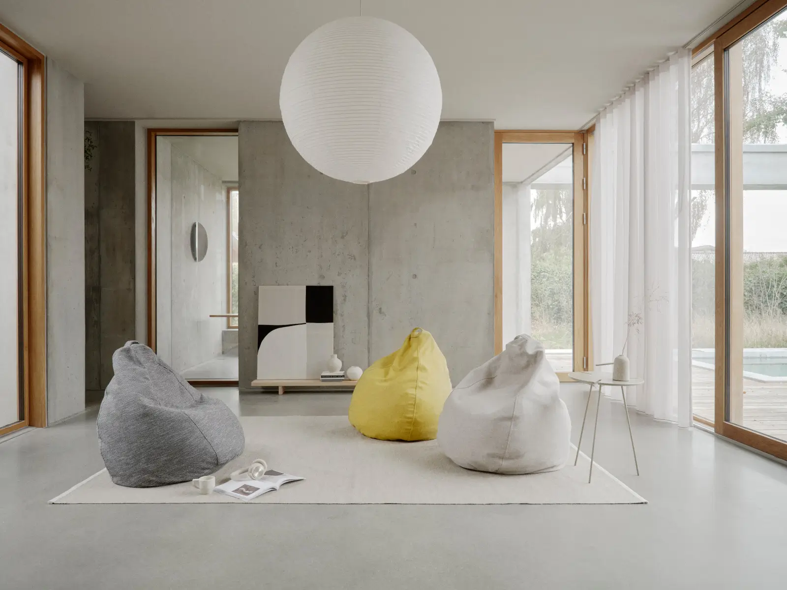 Drei Softline Esprit Sitzsäcke in Grau, Gelb und Hellgrau auf einem Teppich in einem modernen, lichtdurchfluteten Wohnraum mit großen Fenstern.