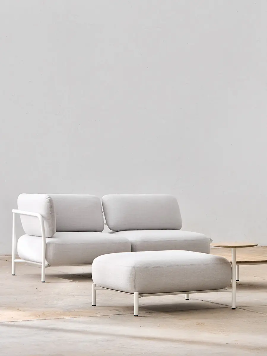 Softline Club Hocker in Hellgrau vor passendem Sofa in einem reduzierten Lounge-Ambiente mit hellem Boden und kleinen Holztischen.