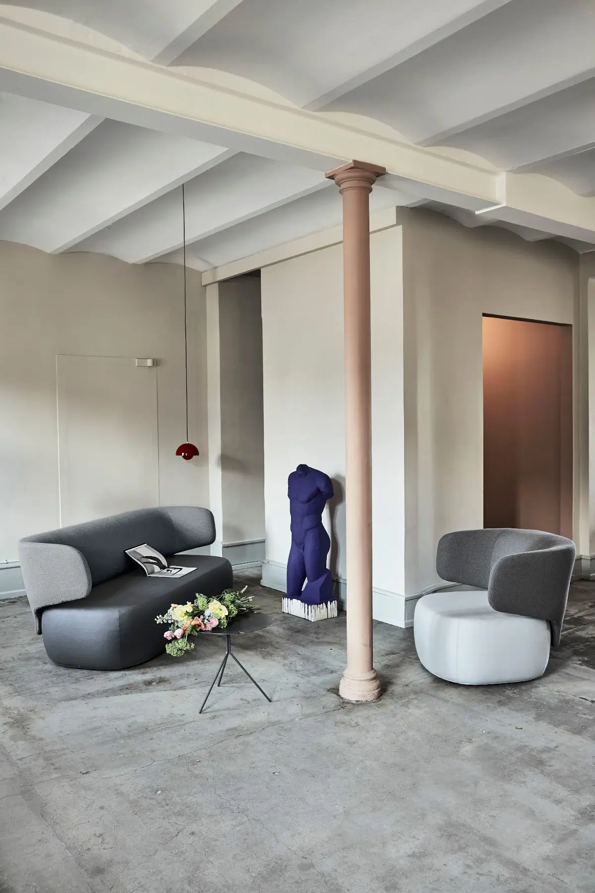 Softline Basel Sofa in Grau zusammen mit einem Basel Sessel in einem modernen Loft mit Betonboden, Beistelltisch und Skulptur.