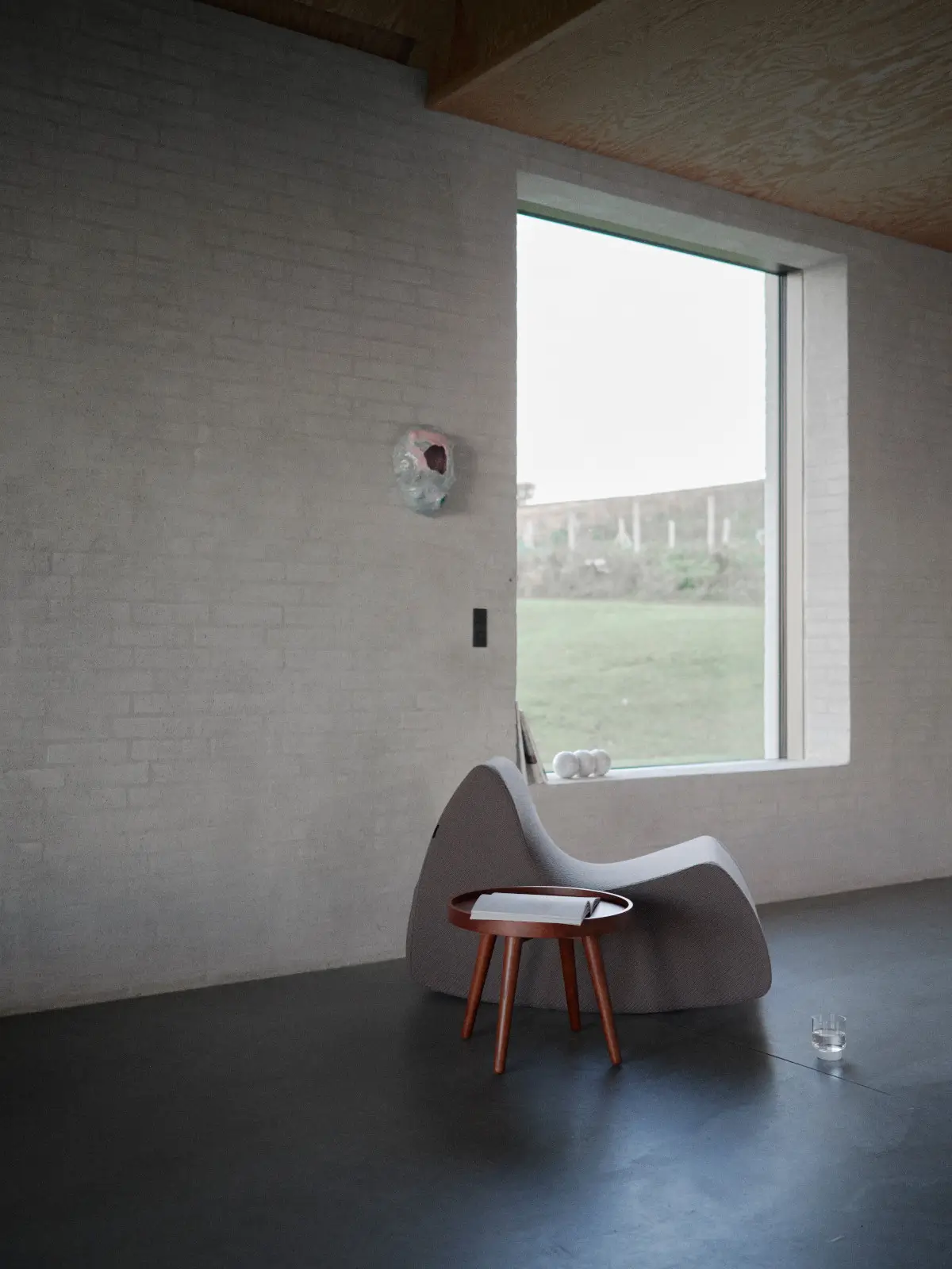 Softline Grand Prix Sessel Large in Grau in einem minimalistischen Wohnambiente mit dunklem Boden, hellem Sichtmauerwerk, großem Fenster und kleinem Holztisch.