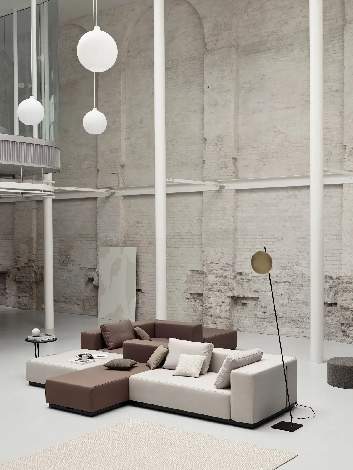 Softline Nevada Hocker in einer großzügigen modularen Sitzlandschaft in Beige und Braun mit Kissen, Teppich und Stehleuchte in modernem Lounge-Ambiente.