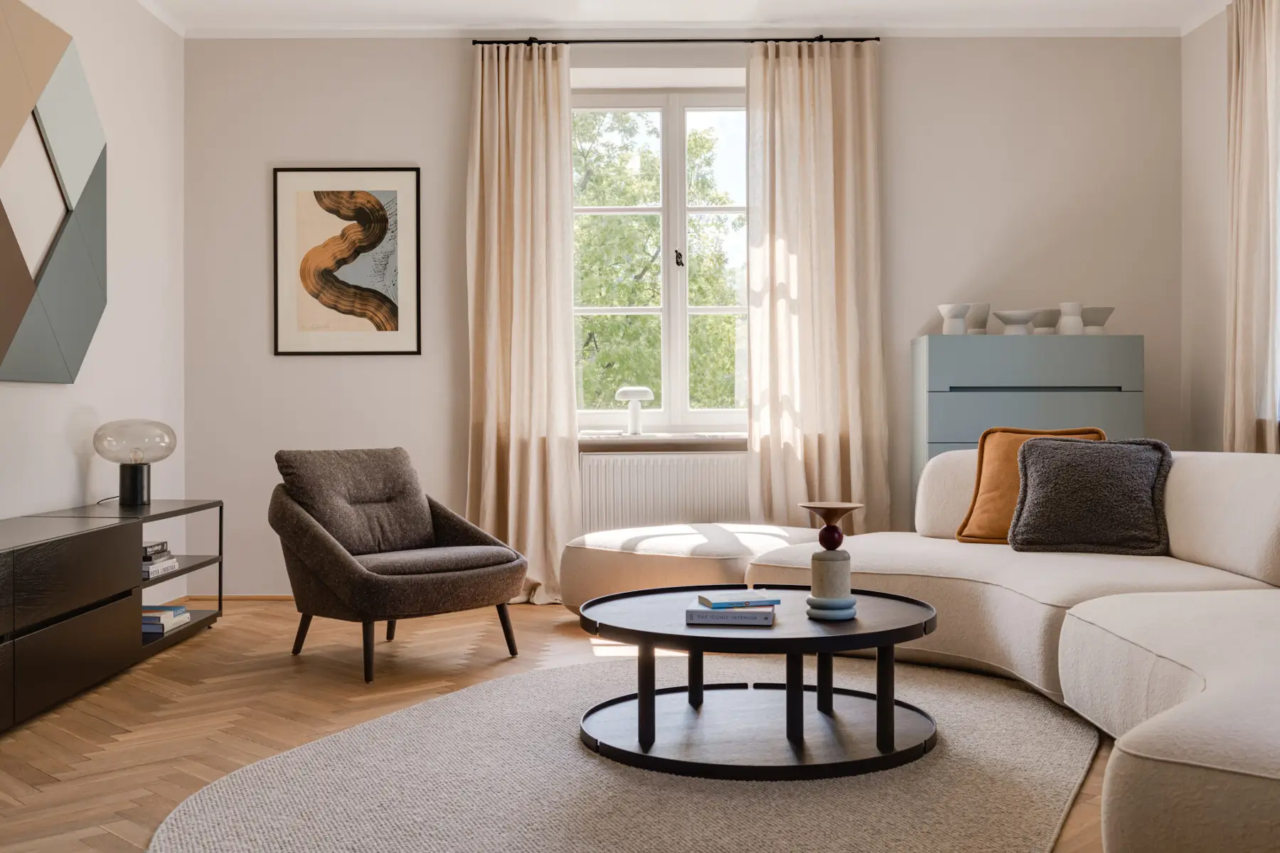 Dunkelgrauer Noti Nome Sessel mit schwarzen Holzbeinen in einem hellen Wohnzimmer mit cremefarbenem Sofa und rundem Couchtisch