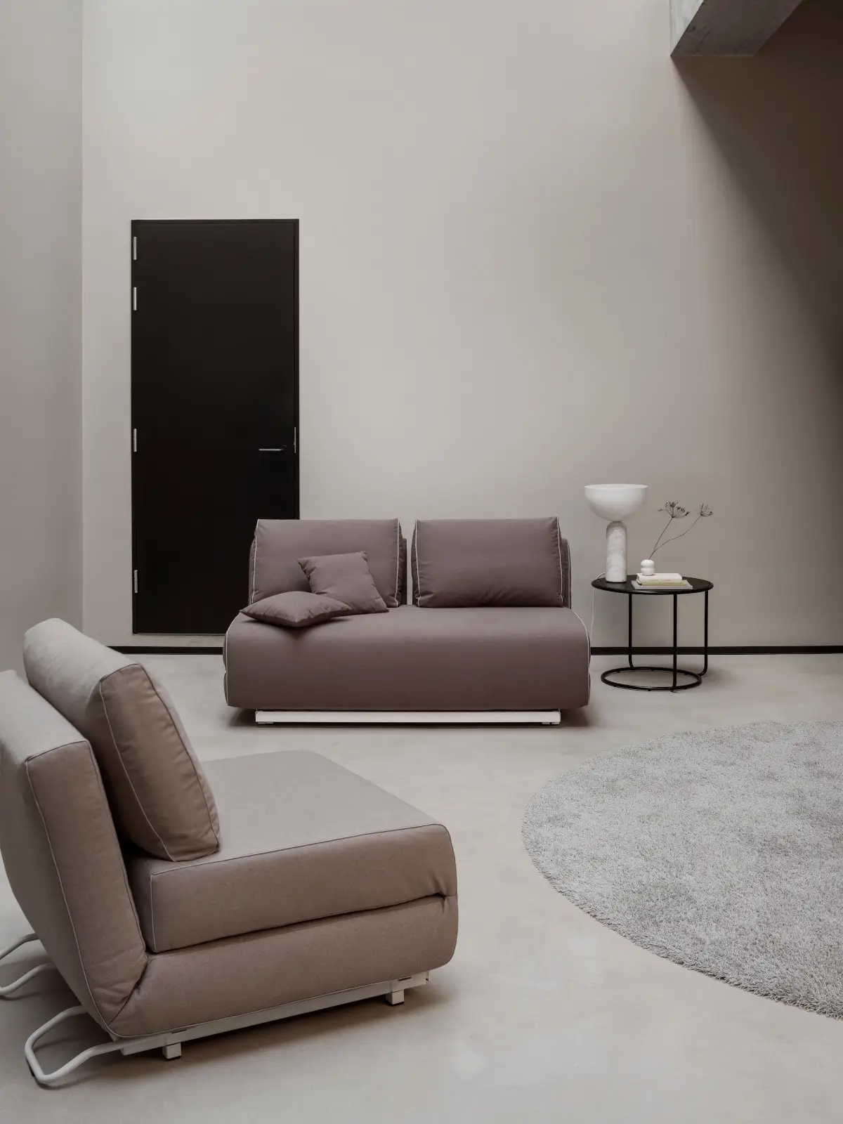 Zwei Softline City Sessel in warmen Beige- und Brauntönen in einem modernen Wohnambiente mit rundem Teppich und schwarzem Beistelltisch.