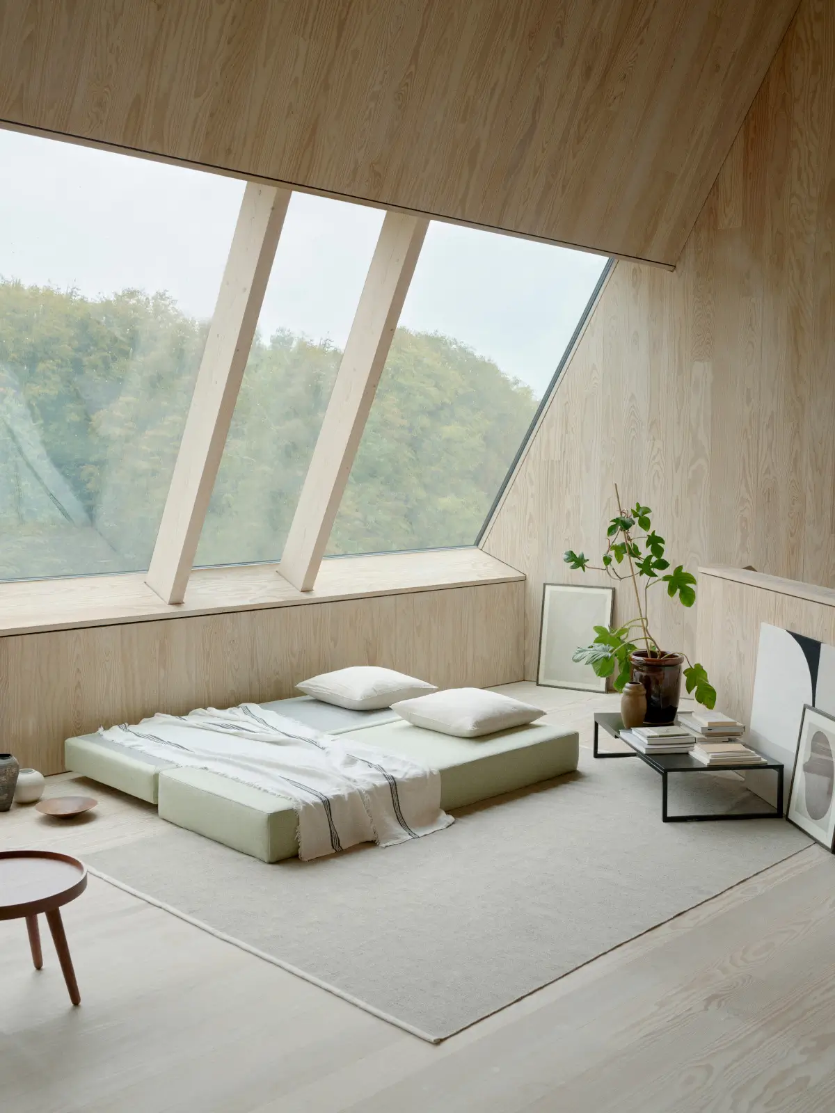 Softline Lubi Daybed in Hellgrün als großzügige Liegefläche mit Kissen und Decke in einem hellen Wohnraum mit Holzverkleidung und großer Fensterfront.