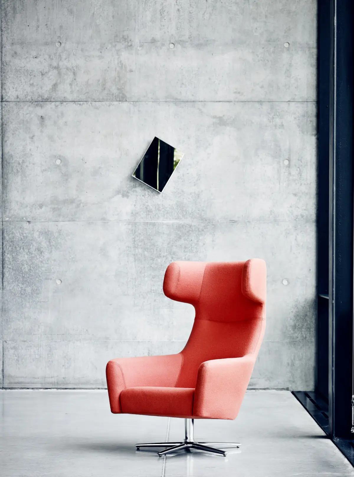 Softline Havana Drehsessel in Orange mit hoher Rückenlehne, seitlichen Kopfstützen und Metall-Kreuzfuß in modernem Ambiente vor einer Betonwand.