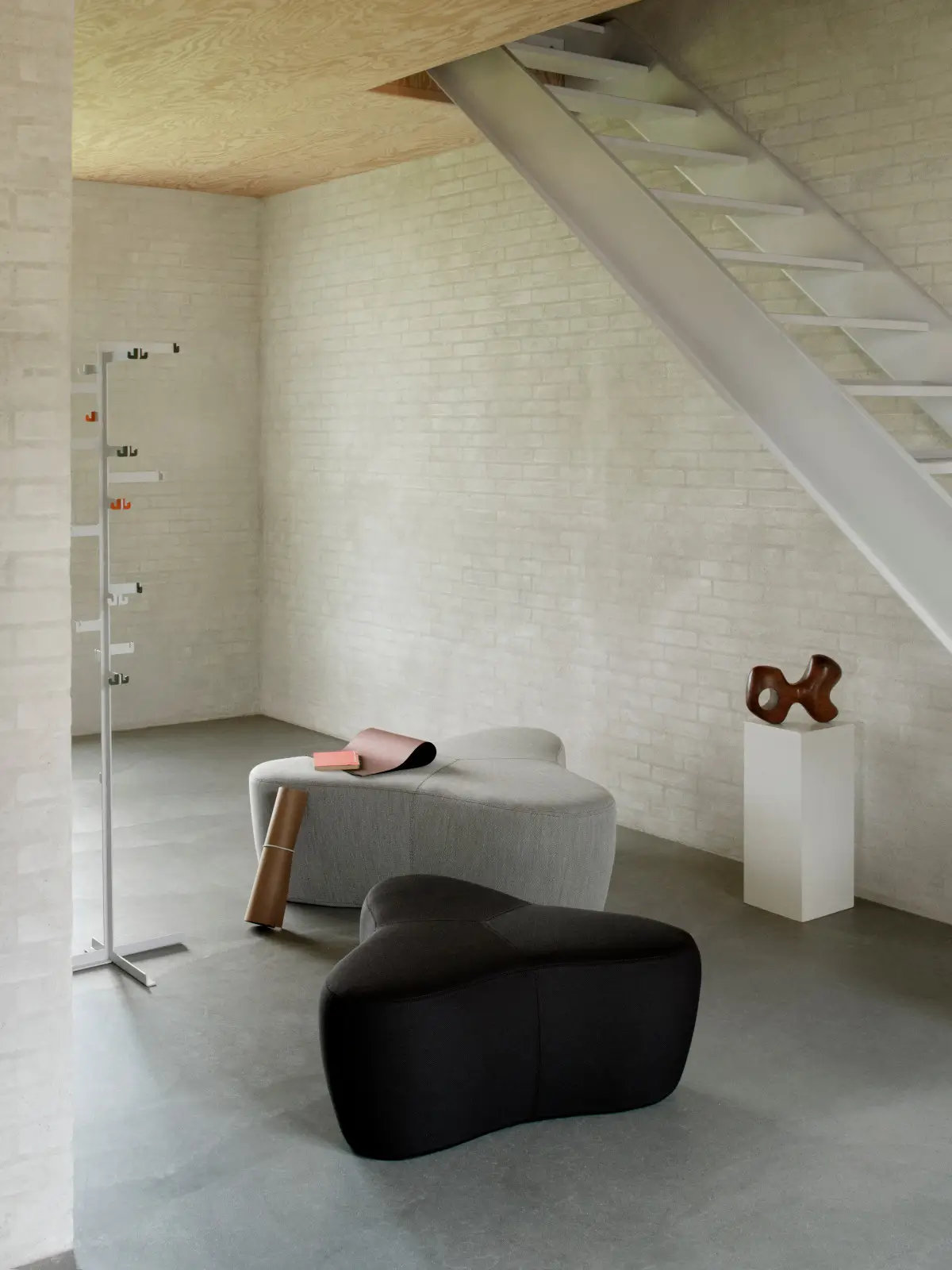 Softline Chat Hocker Small in Schwarz und Hellgrau in einem modernen Wohnambiente mit heller Ziegelwand, Treppe und minimalistischer Einrichtung.