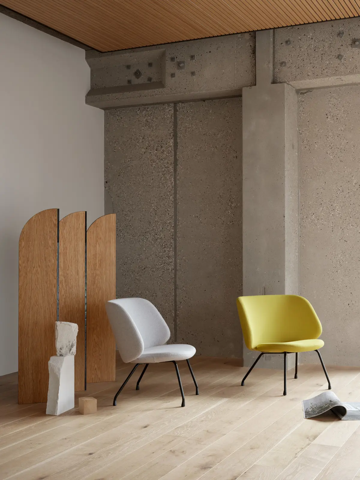 Zwei Softline Evy Sessel in Grau und Gelb mit schwarzem Metallgestell in einem modernen Wohnambiente mit Holzboden, Betonwand und Raumteiler.