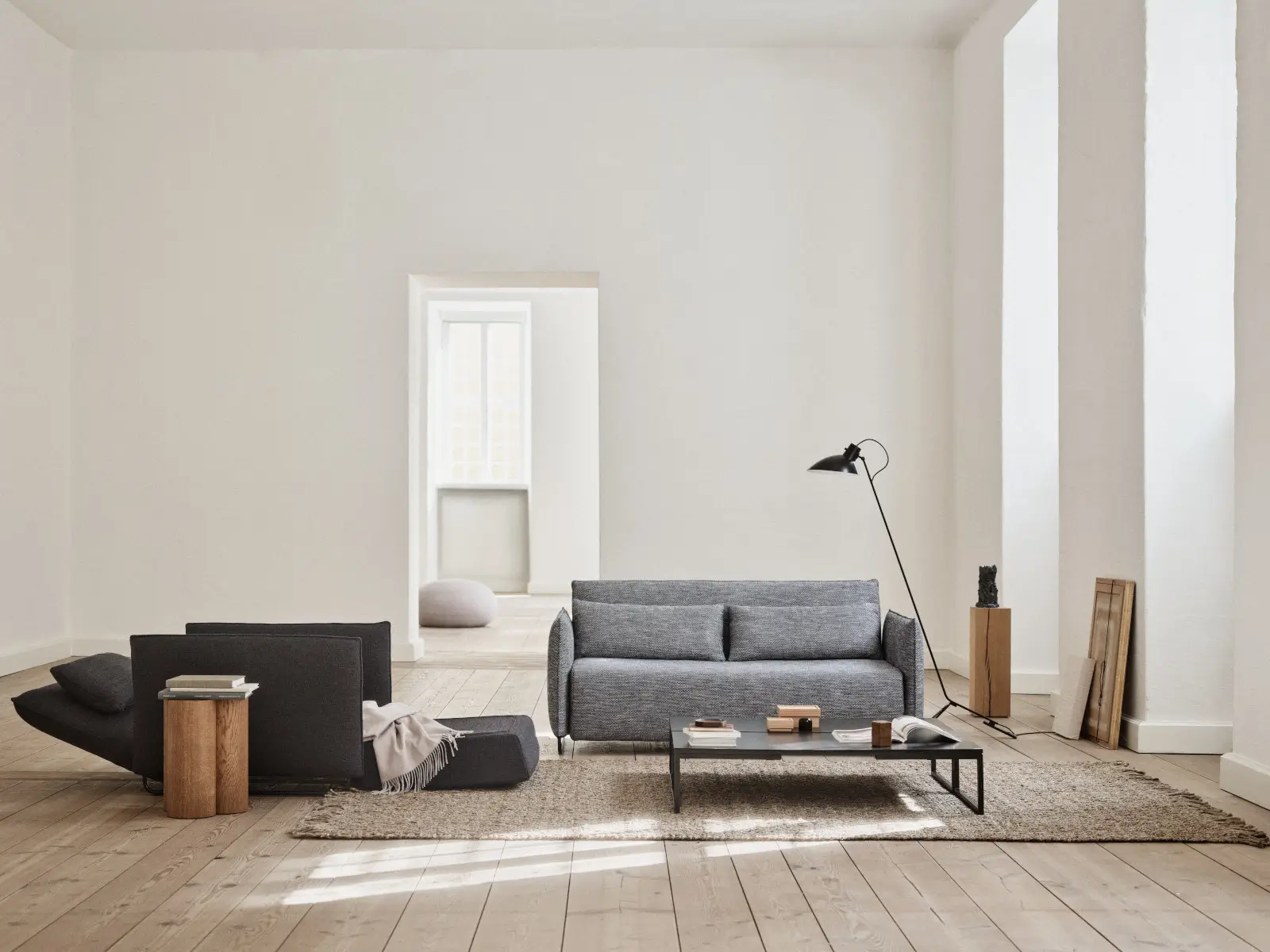 Softline Cord Sessel in Dunkelgrau mit ausgeklappter Liegefläche neben einem grauen Sofa in einem hellen Wohnraum mit Holzboden und Teppich.