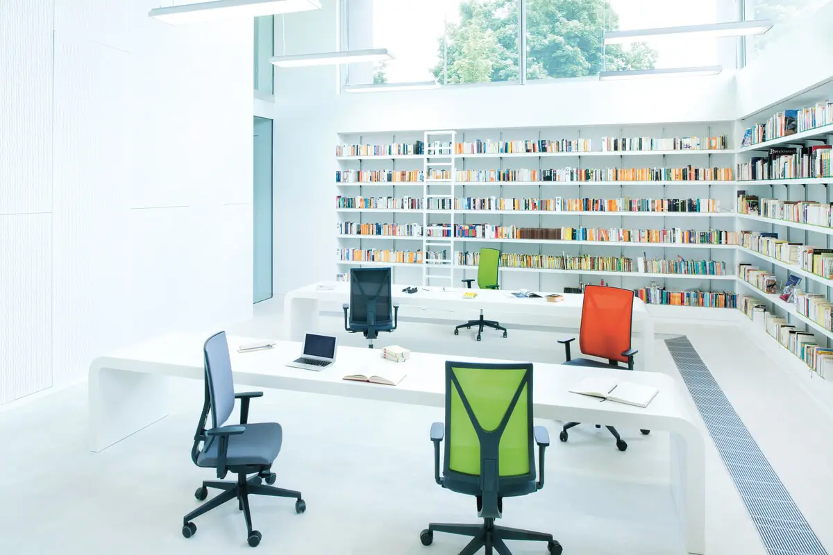 Girsberger Yanos Drehstuhl mit Netzrücken an Arbeitsplätzen in einer hellen Bibliothek mit Bücherregalen.