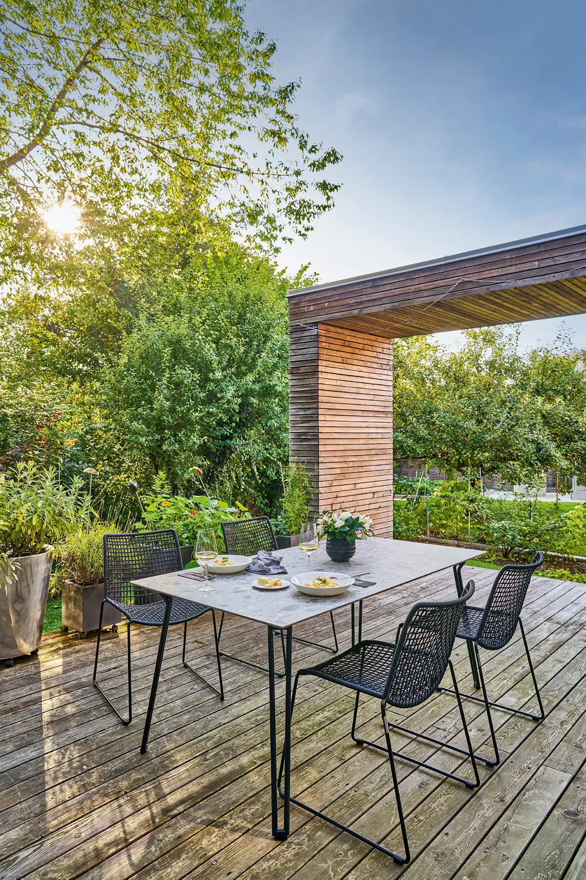 Weishäupl Slope Sitzgruppe mit schwarzem Esstisch und Gartenstühlen auf einer modernen Holzterrasse. Wetterfeste Outdoor-Designmöbel für Garten und Terrasse.