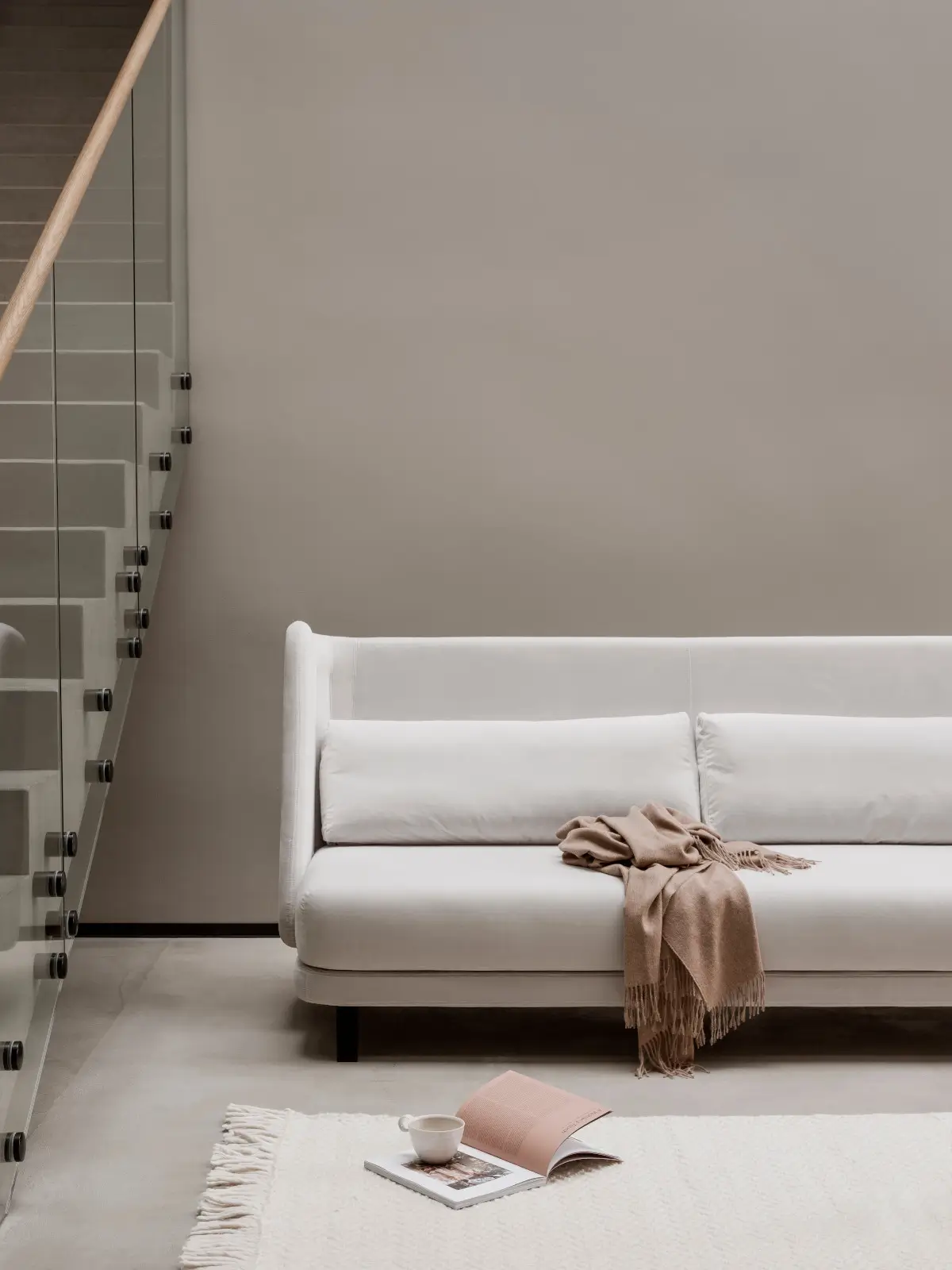 Softline Jason Sofa in Weiß mit zwei Rückenkissen und beigefarbener Decke in einem modernen Wohnbereich mit Glastreppe und hellem Teppich.