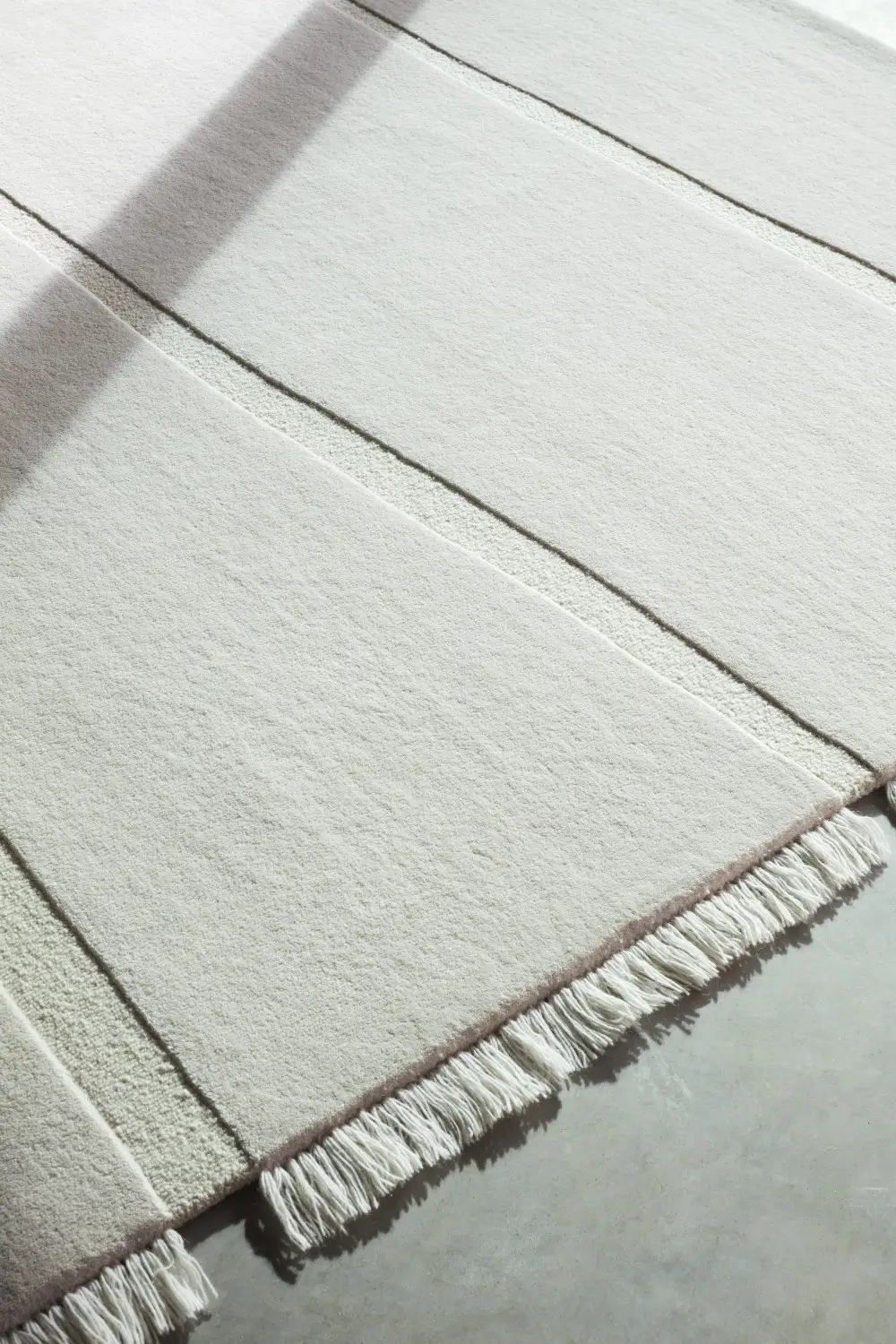 Massimo Copenhagen Atoll Teppich in Cream aus der Nähe mit weicher, heller Oberfläche, schmalen Strukturstreifen und Fransen am Teppichrand.
