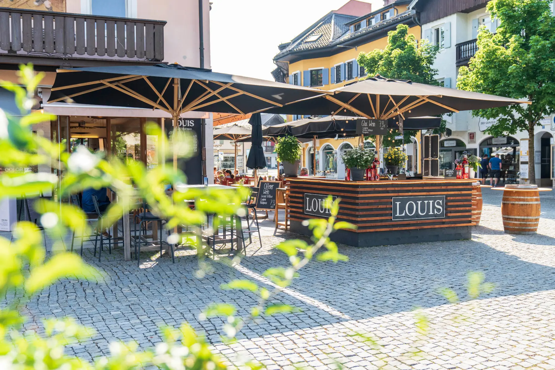 Mehrere Weishäupl Klassiker Schirme 300 x 300 cm in Schwarz auf einer Außenterrasse eines Cafés