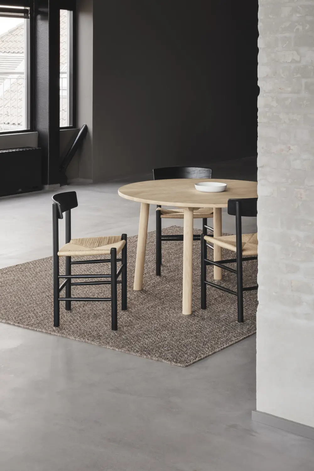 Massimo Copenhagen Belize Teppich in Taupe unter einem runden Holztisch mit schwarzen Stühlen und geflochtenen Sitzflächen in einem modernen Essbereich.