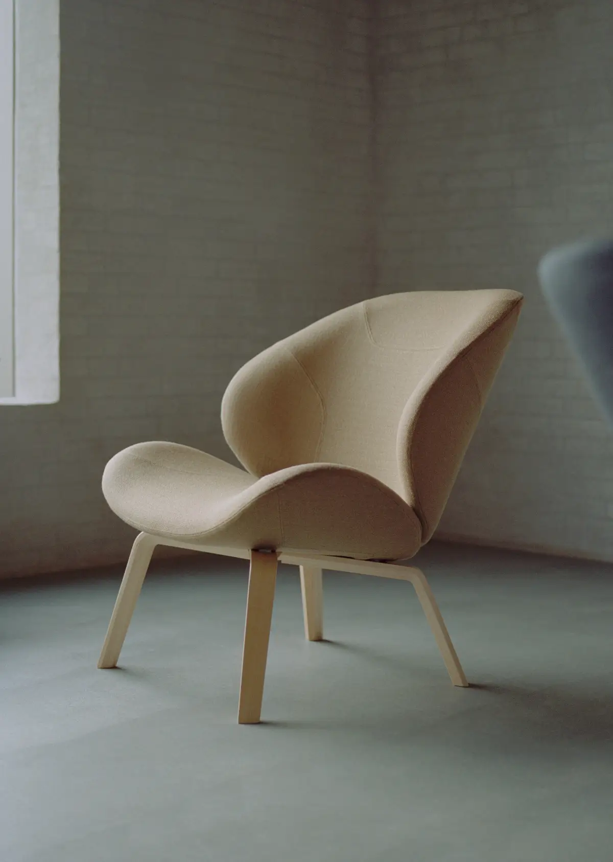Softline Eden Sessel in Beige mit hellem Holzgestell in einem reduzierten Wohnambiente vor grauer Wand.
