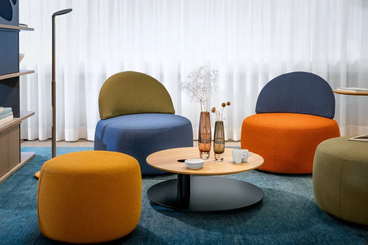 Girsberger Tala Rundtisch als niedriger Tisch zwischen farbigen Loungesesseln und Hockern.