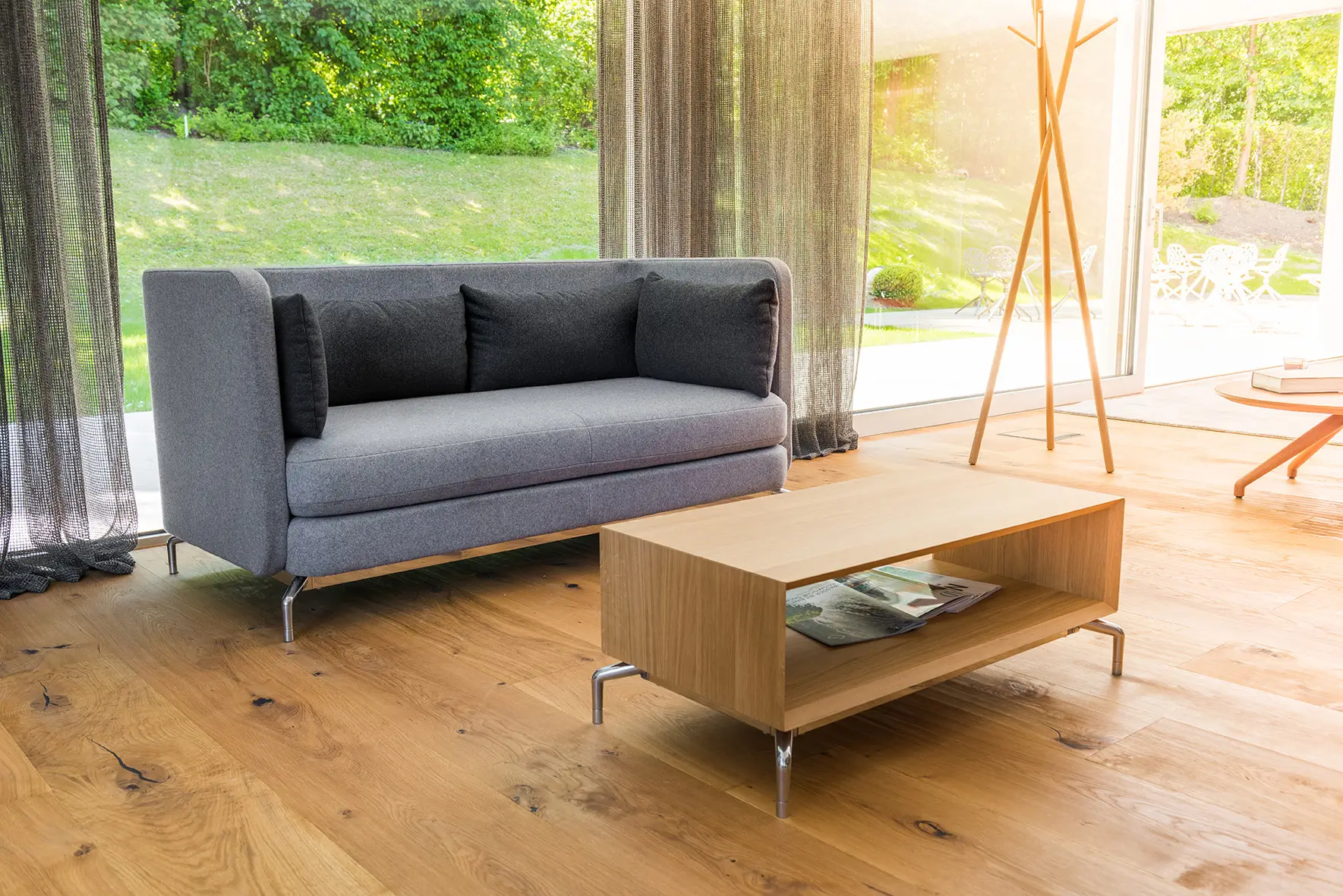 Wagner W-Lounge Low Sofa mit hellgrauer Polsterung und schwarzen Kissen in einem modernen Wohnzimmer mit bodentiefen Fenstern und Holzboden.