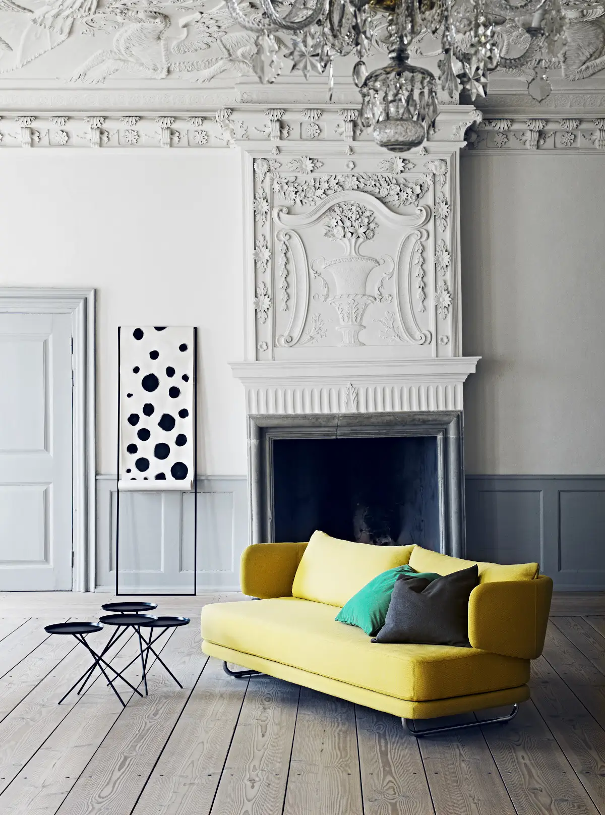 Softline Jasper Sofa in Gelb mit farbigen Kissen in einem eleganten Wohnambiente vor einem verzierten Kamin mit Holzboden und Beistelltischen.