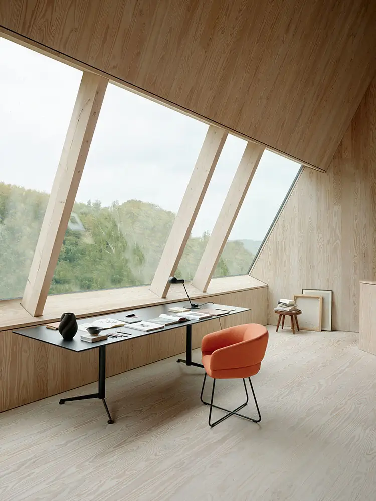 Softline Caleto Loungesessel in Orange mit schwarzem Metallgestell in einem großzügigen, hellen Raum mit Holzinterieur, Schreibtisch und großen Fenstern.