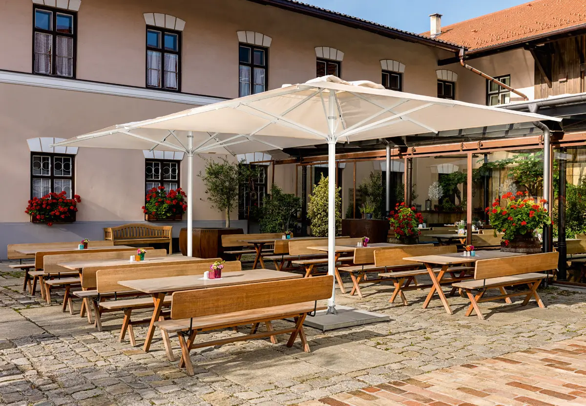 Große Weishäupl Teleskopschirme 400 x 400 cm über einer Gastronomie-Terrasse mit Sitzgruppen und Holzmöbeln