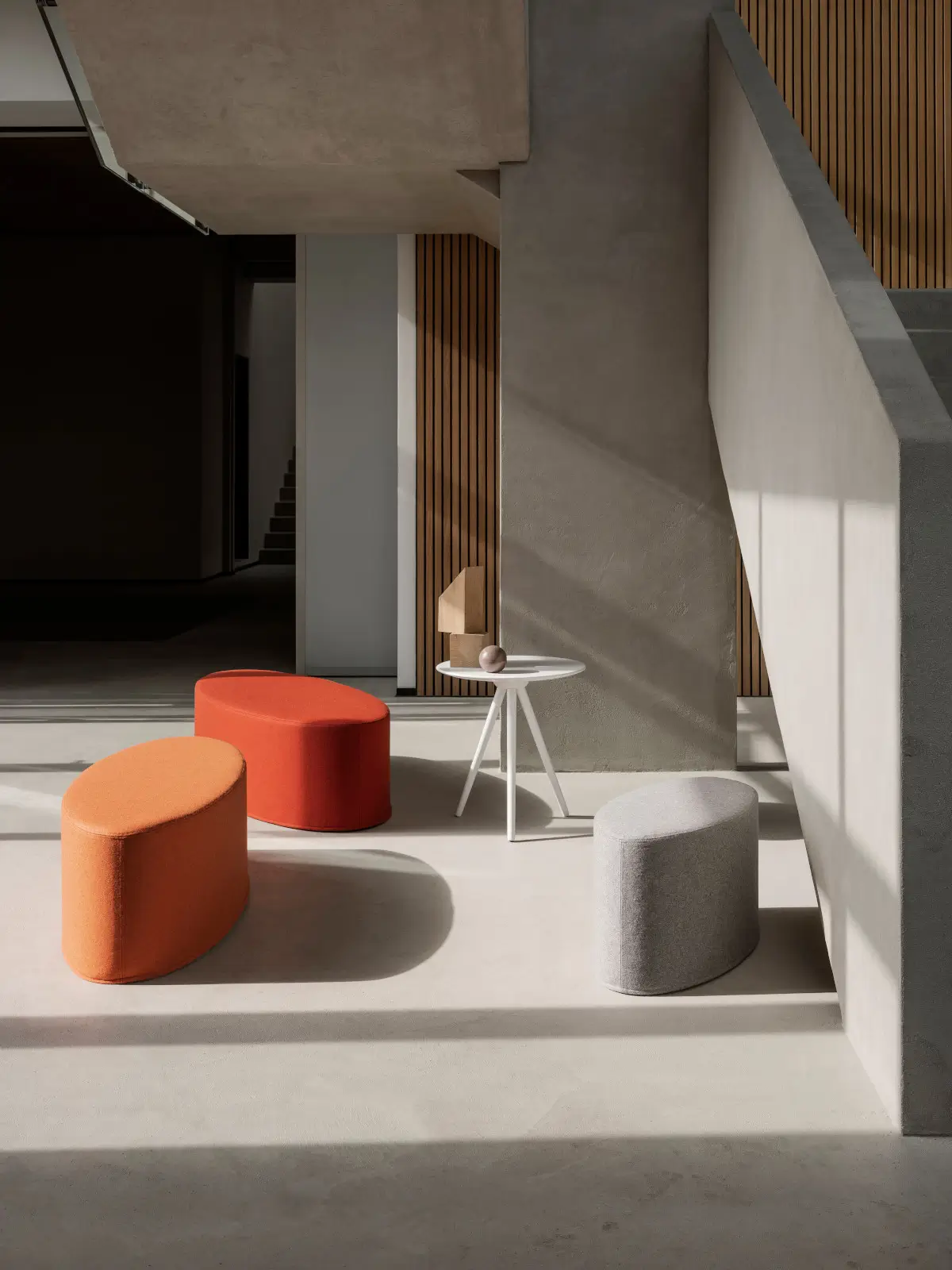 Softline Bon-Bon Hocker Small in Orange, Rot und Hellgrau in einem modernen Wohnambiente mit weißem Beistelltisch und minimalistischer Architektur.