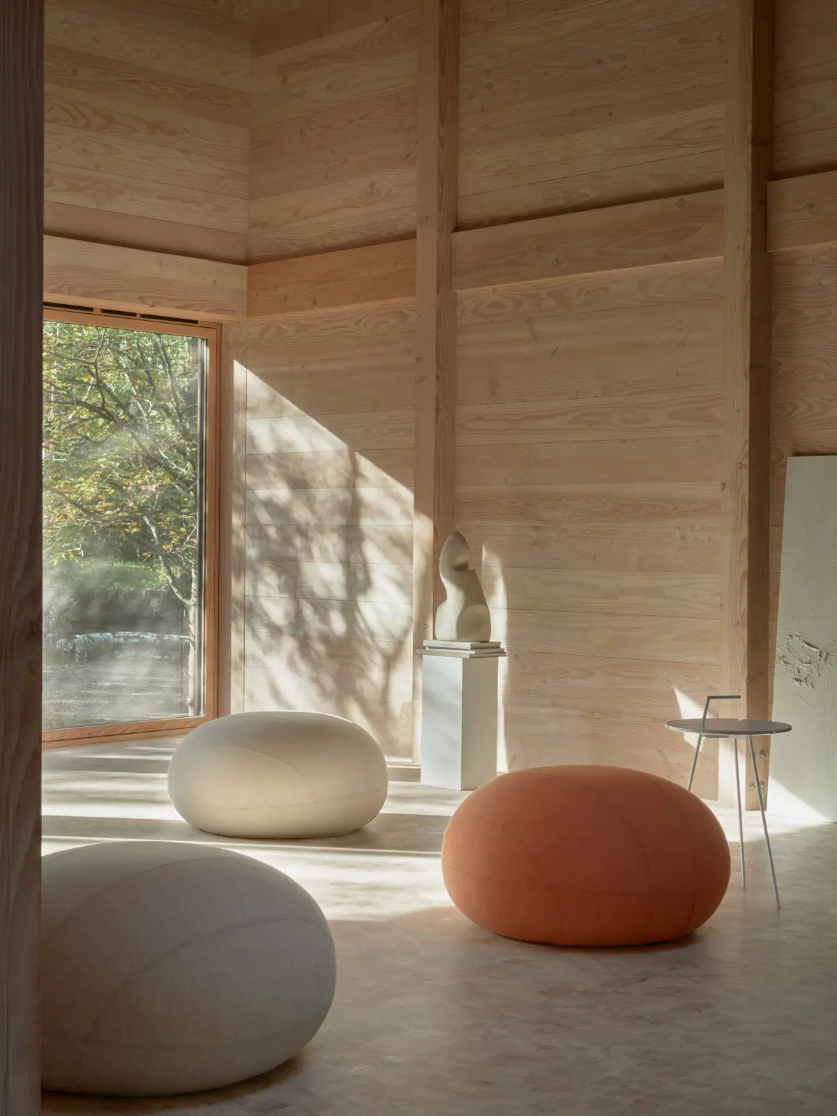 Softline Cut Hocker in Orange und hellen Naturtönen in einem modernen Wohnambiente mit Holzwänden, großen Fenstern und Beistelltisch.