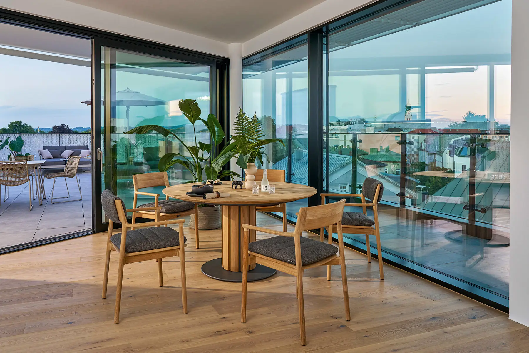 Weishäupl Teva Essgruppe mit rundem Teakholztisch Ø 140 cm und gepolsterten Sesseln in einem modernen Wohnbereich. Hochwertige Designmöbel für innen und außen.