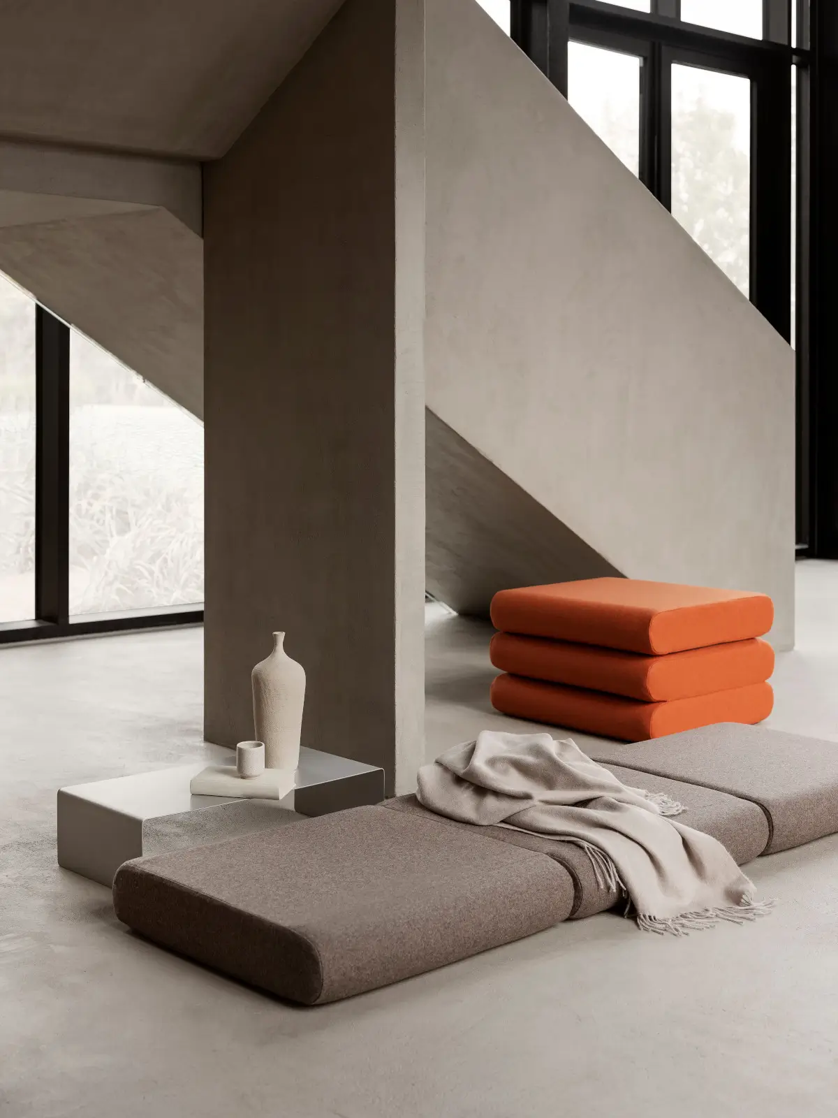 Softline Bingo Hocker in Orange gestapelt in einem modernen Wohnambiente mit grauen Polsterelementen, Decke und Beistelltisch.