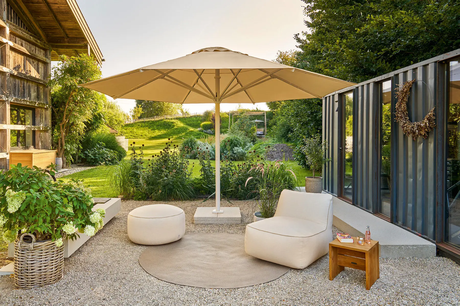 Weishäupl Teleskopschirm mit 500 cm Durchmesser in Pastellapricot über einer stilvollen Gartenlounge mit Loungesessel und Hocker