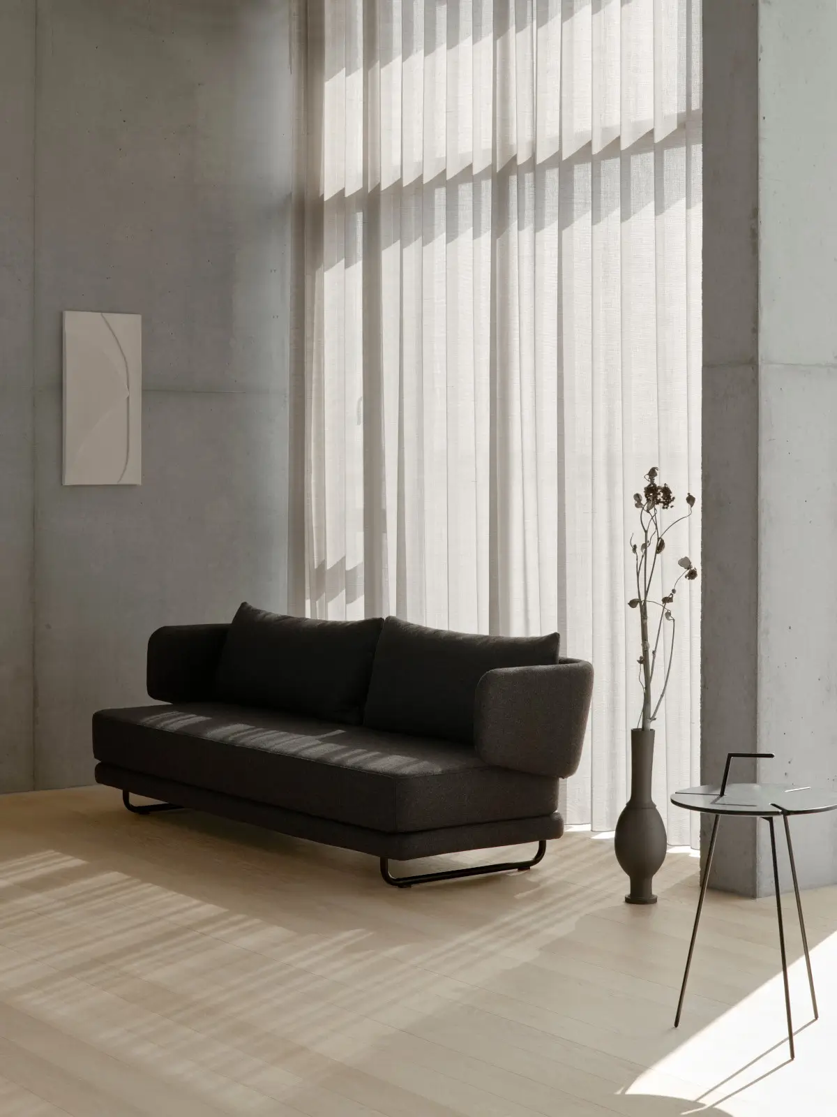Softline Jasper Sofa in Dunkelgrau mit zwei Rückenkissen und gepolsterten Armlehnen in einem modernen, lichtdurchfluteten Wohnambiente.