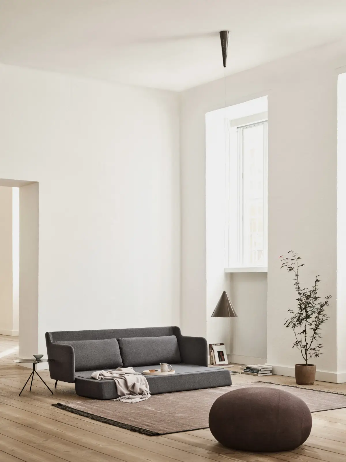 Softline Cut Hocker in Dunkelbraun im Vordergrund eines hellen Wohnambientes mit grauem Sofa, Teppich, Holzboden und Beistelltisch.