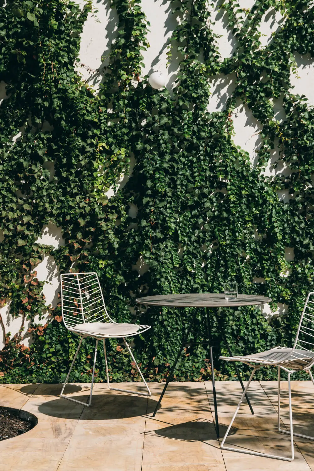 Arper Leaf Bistrotisch mit runder Tischplatte, schlanken Metallbeinen und stabilisierenden Querstreben auf einer Terrasse.