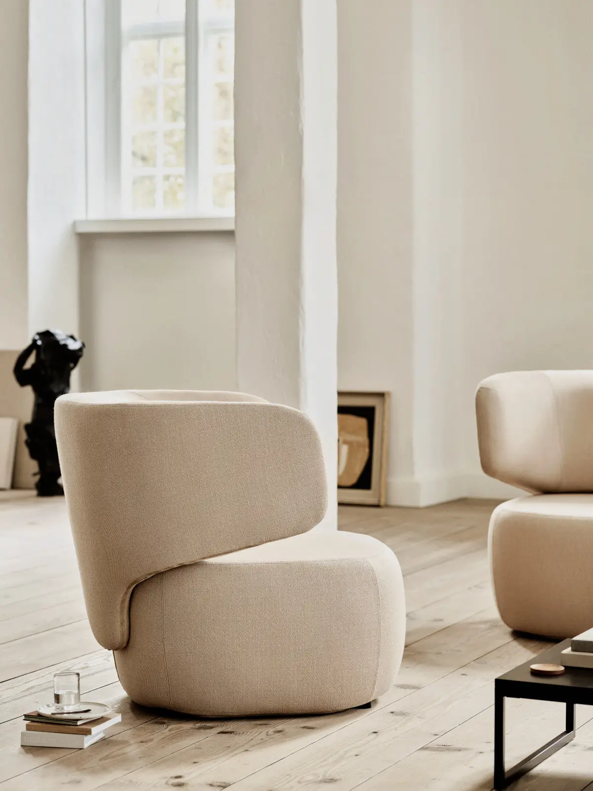 Softline Basel Sessel in Beige aus seitlicher Perspektive in einem hellen Wohnraum mit Holzboden, Beistelltisch und Wohnaccessoires.