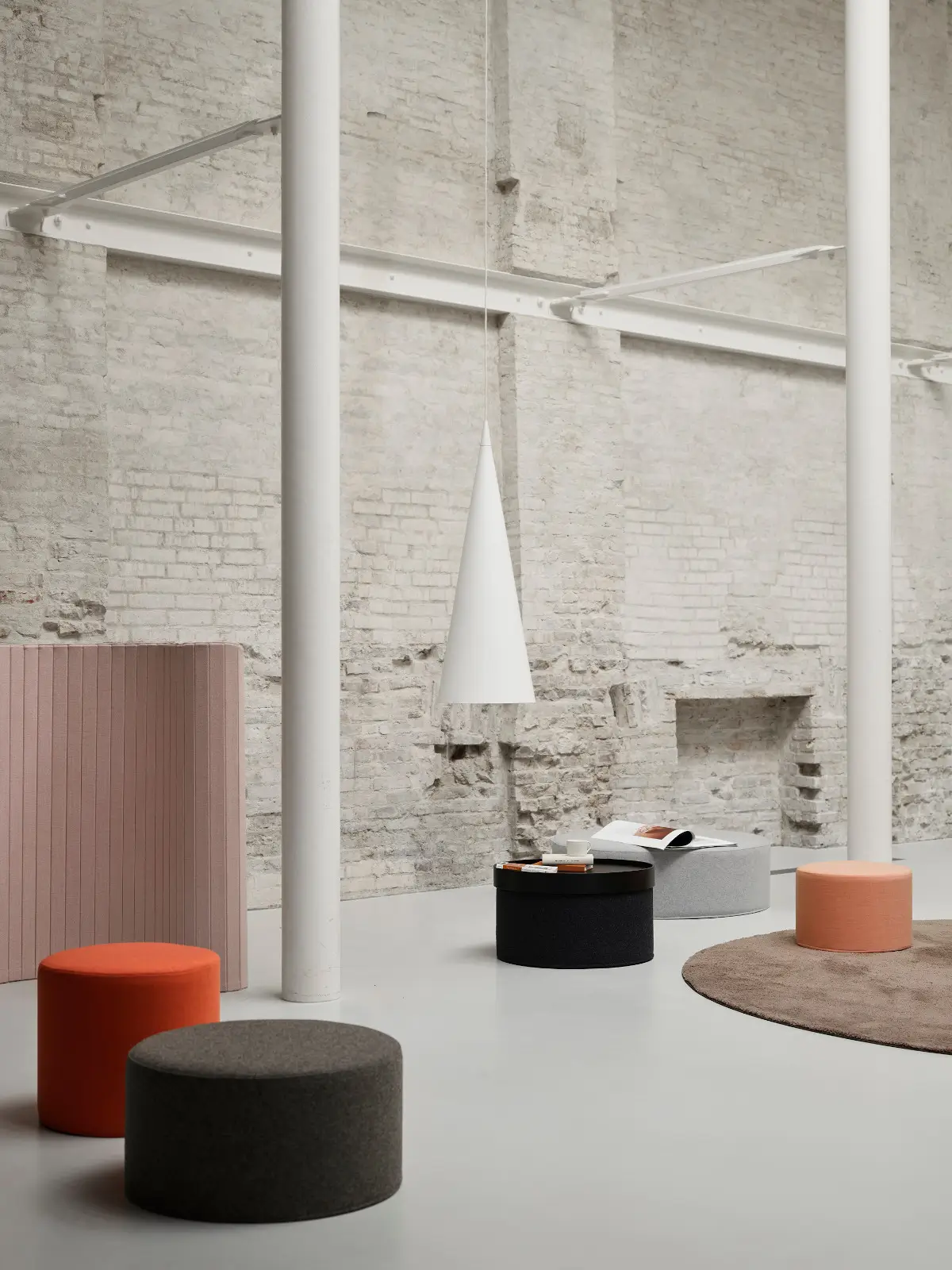 Mehrere Softline Drum Hocker in Orange, Dunkelgrau, Grau und Apricot in einem hellen, modernen Wohnambiente mit Backsteinwänden und rundem Teppich.