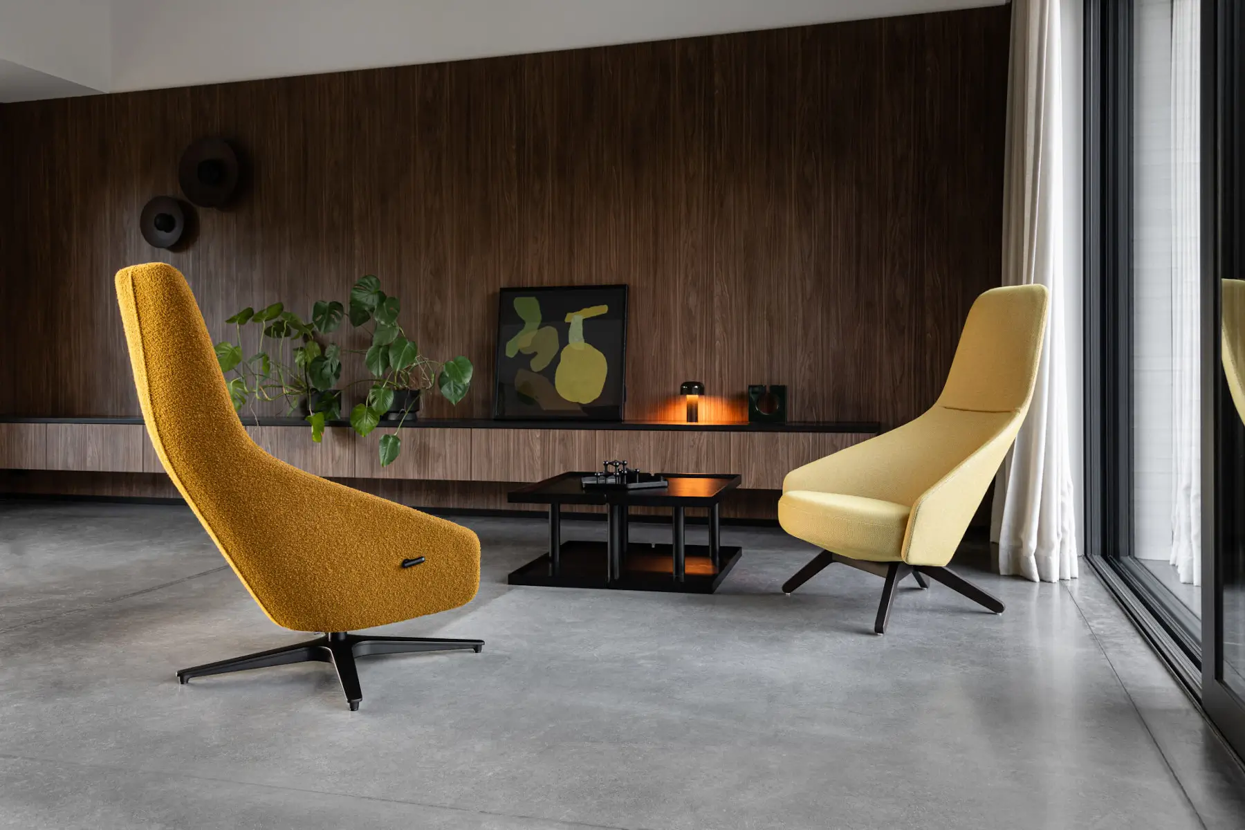 Zwei Noti Palo Sessel in Gelbtönen mit hohen Rückenlehnen und dunklen Gestellen in einer modernen Lounge mit Beistelltisch