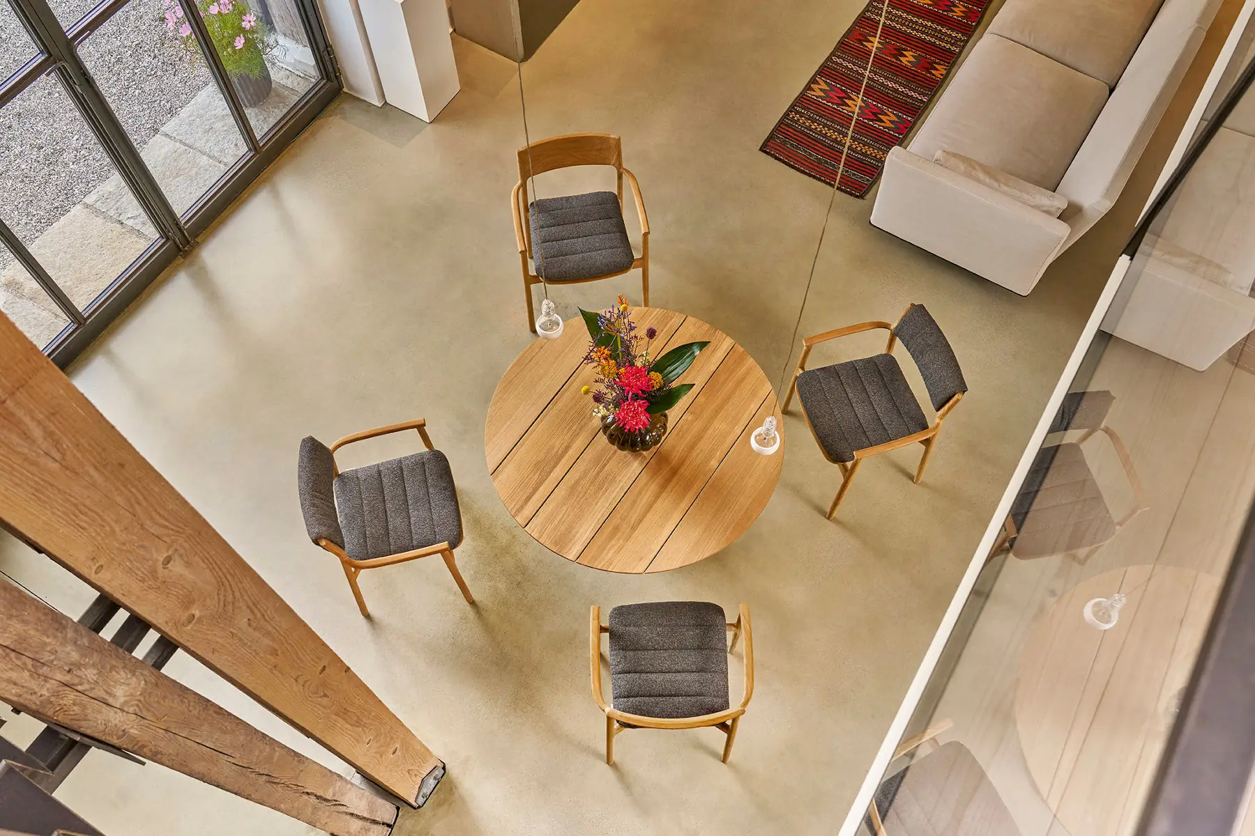 Weishäupl Teva Essgruppe mit rundem Teakholztisch Ø 120 cm und gepolsterten Sesseln in einem offenen Wohn- und Essbereich. Zeitloses Design für innen und außen.