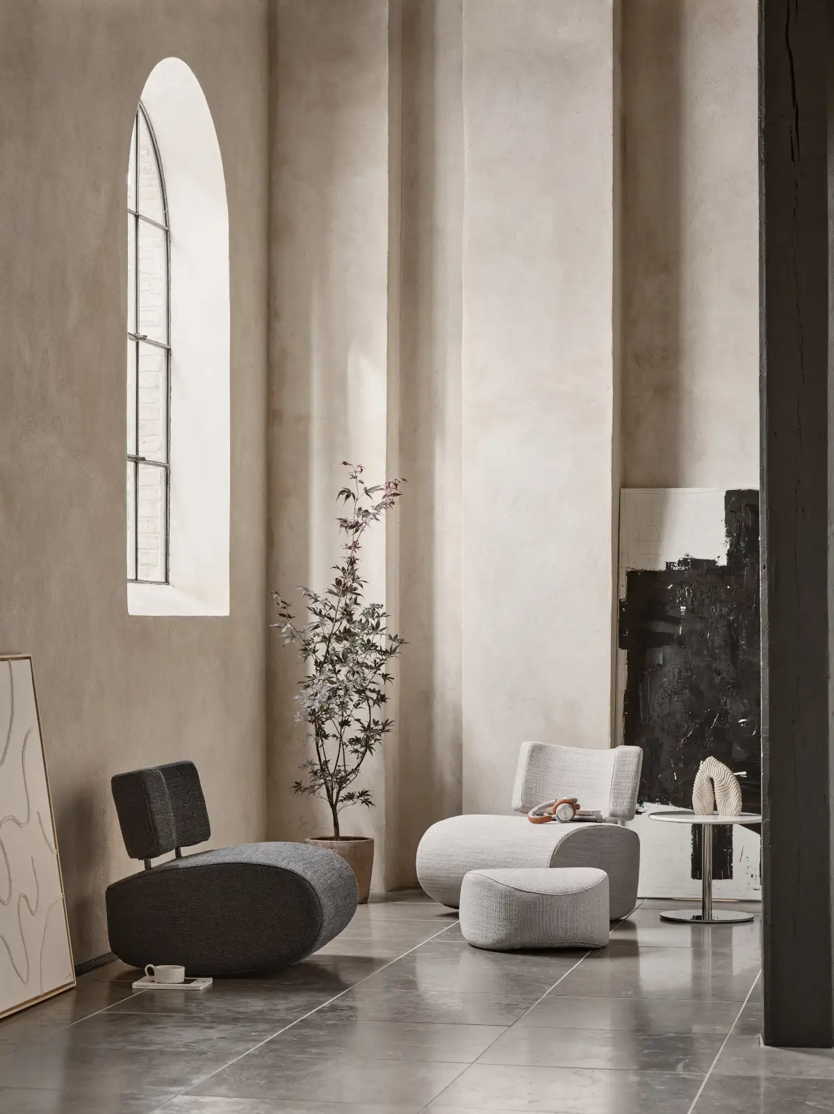 Softline Apollo Sessel in Grau und Hellgrau mit passenden Hockern in einem modernen Wohnambiente mit hohen Fenstern, Pflanze und Beistelltisch.