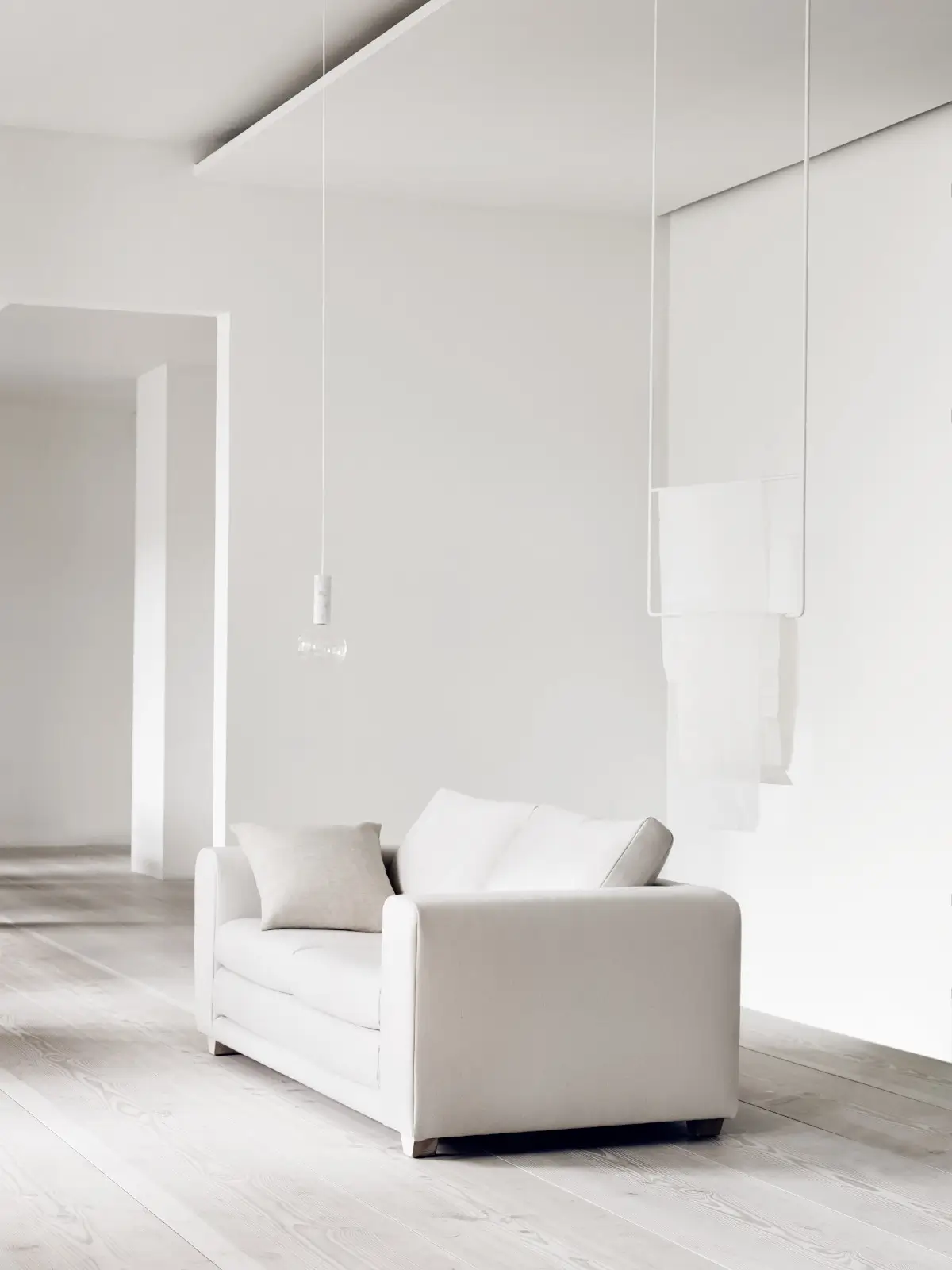 Softline Victor Sofa 2,5-Sitzer in Weiß mit hellem Kissen in einem minimalistischen Wohnambiente mit weißen Wänden und hellem Holzboden.