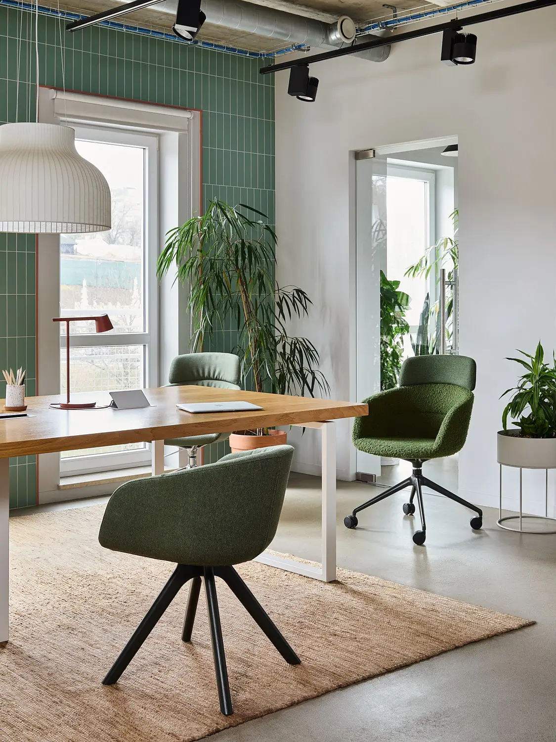 Noti Paxt Soft Stuhl mit grüner Polsterung und dunklen Holzbeinen an einem Schreibtisch im modernen Büro mit weiteren Sitzmöbeln